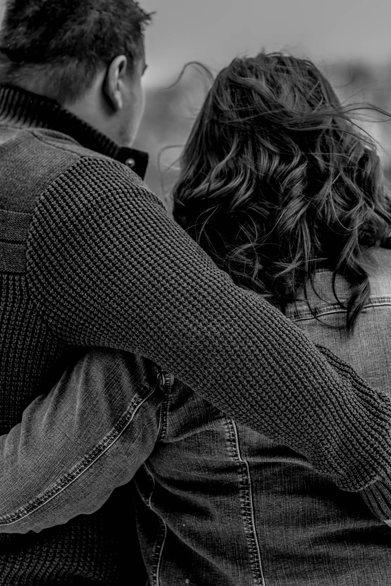 Black and white close-up of couple in denim and knit sweaters embracing.