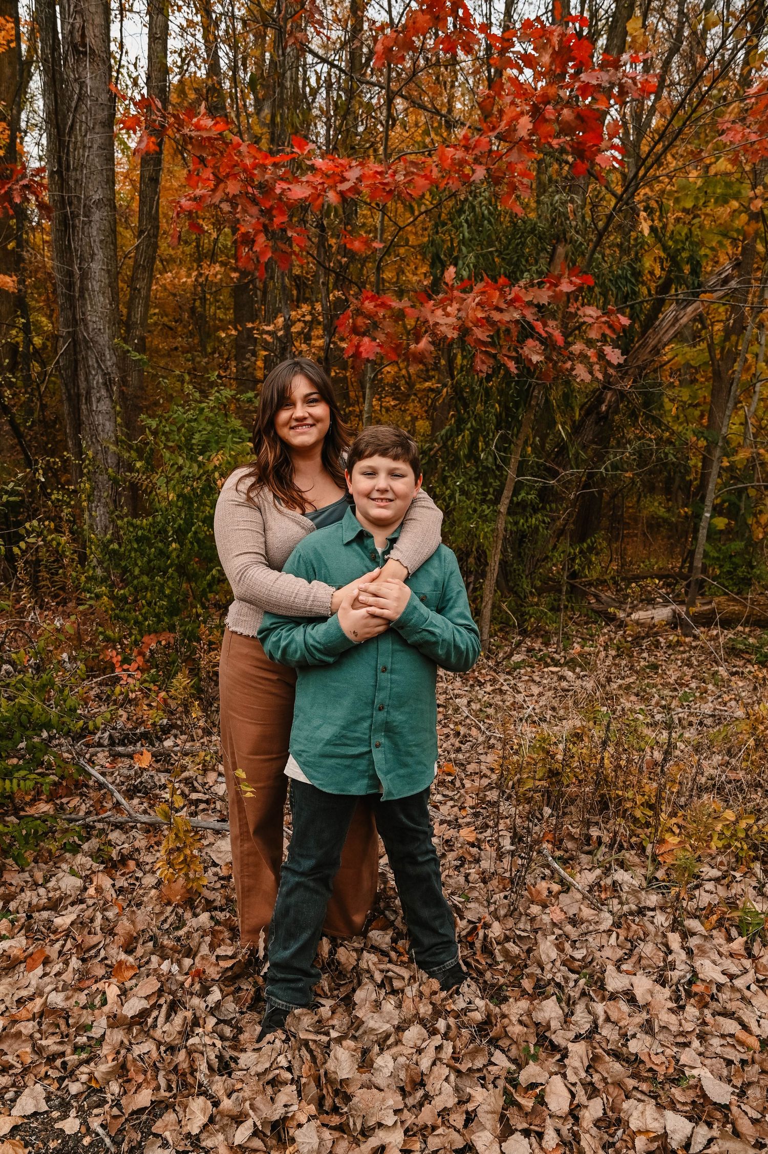 Playful embrace captured against vibrant fall foliage in the woods.