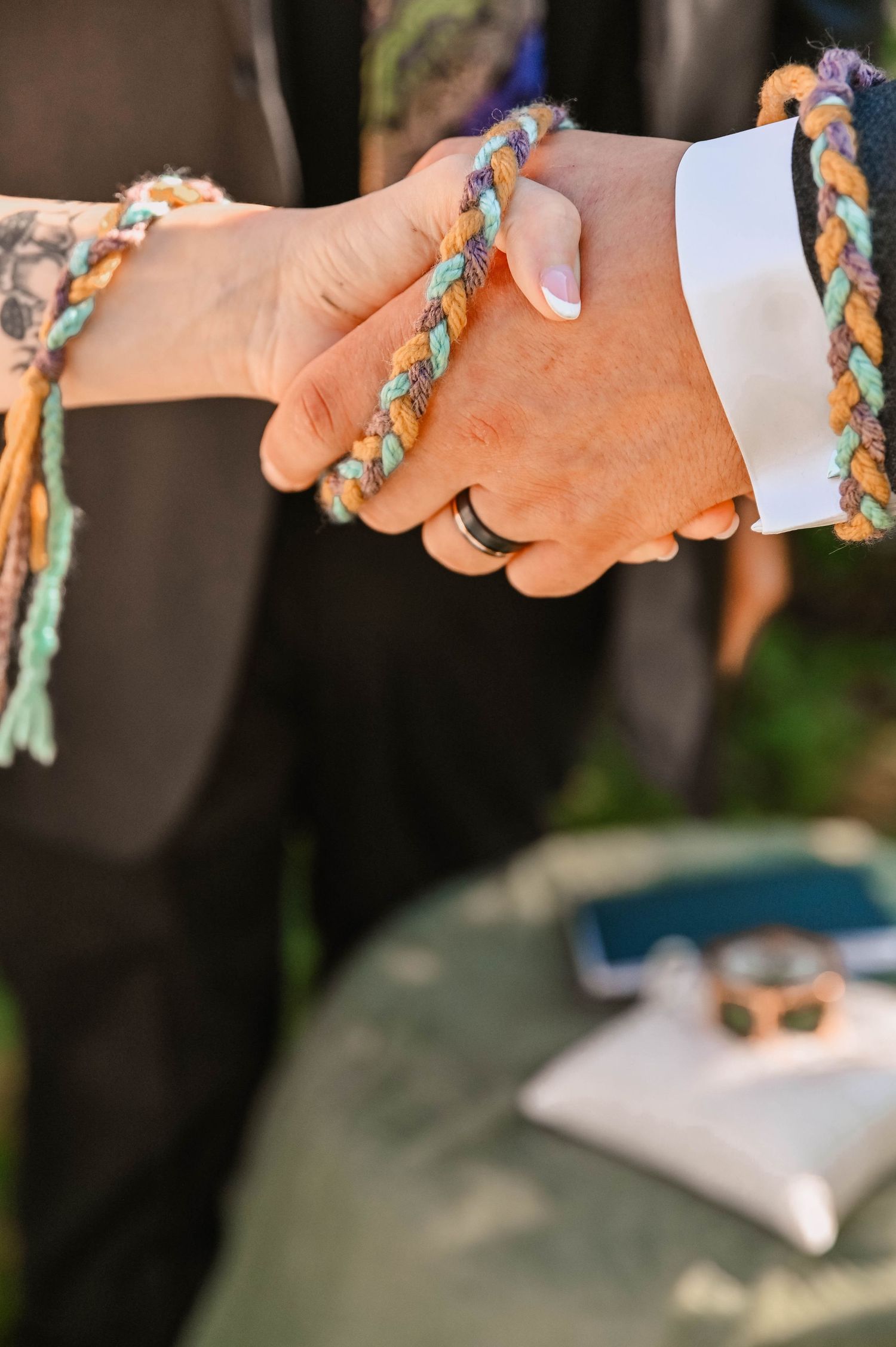 Hands joined in a handfasting ceremony with colorful braided cords.