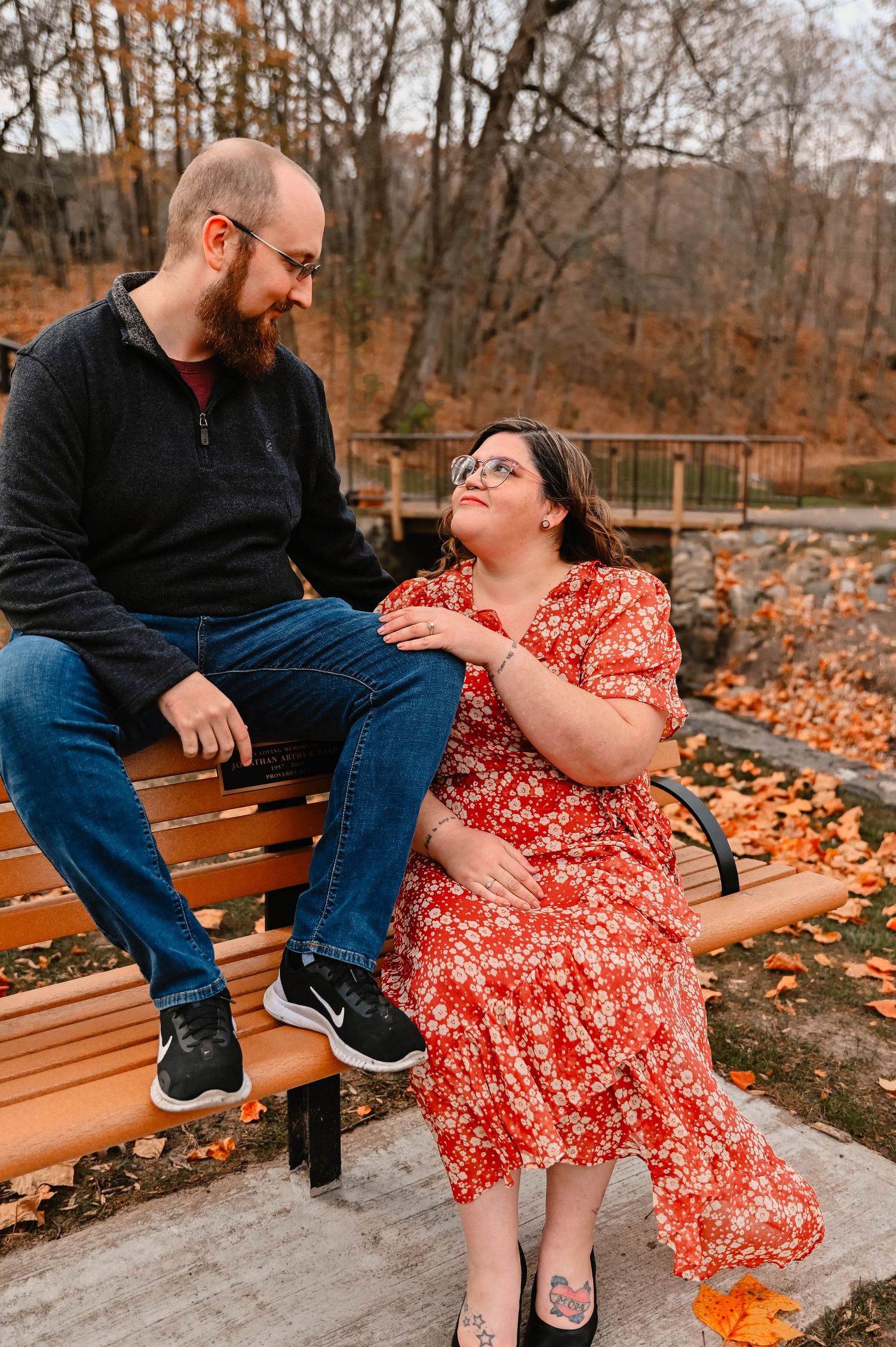 Couple sharing a playful moment on a wooden bench surrounded by fall foliage.