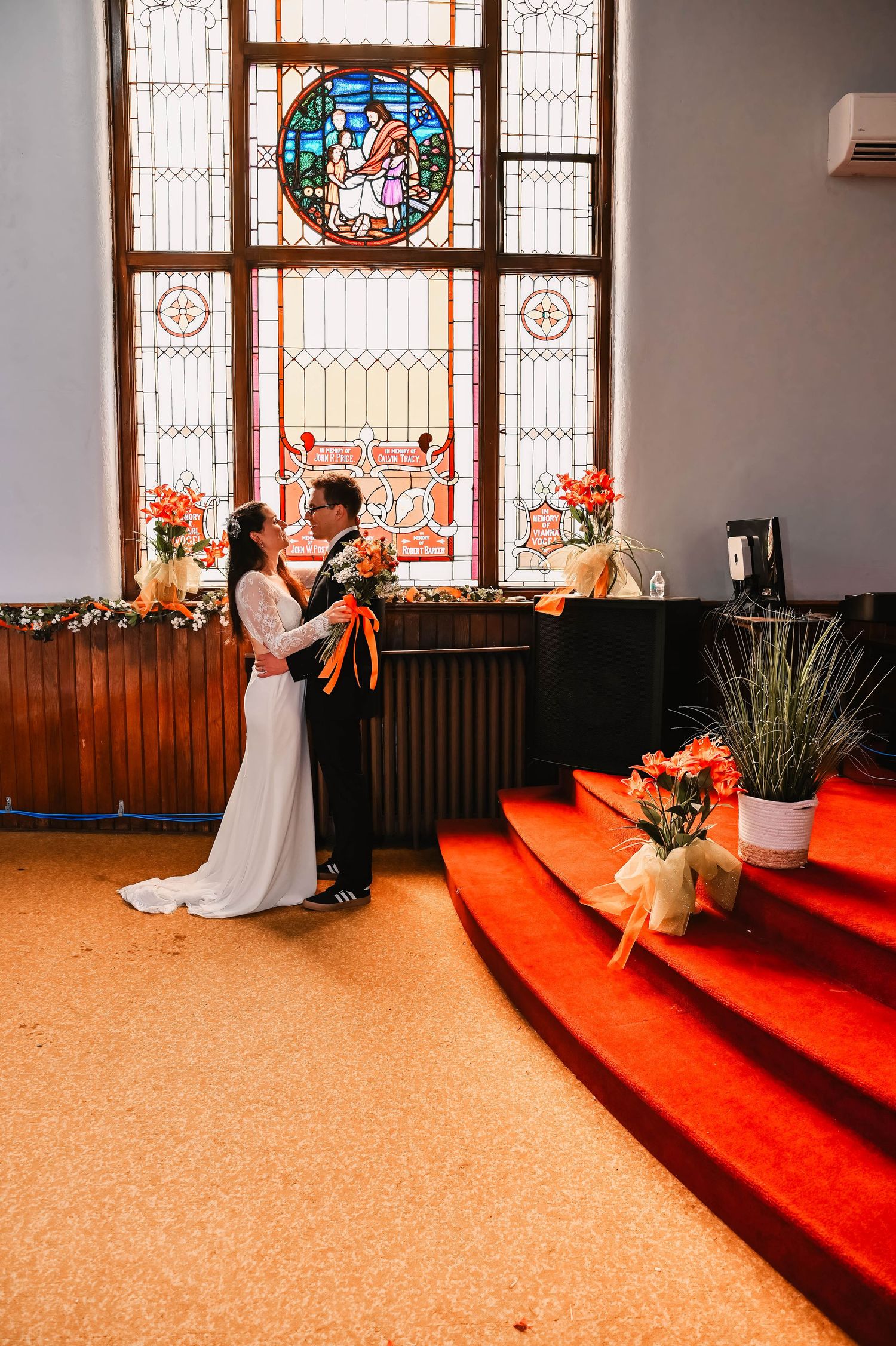 A wedding ceremony in a church with beautiful stained glass windows and red carpeted steps.