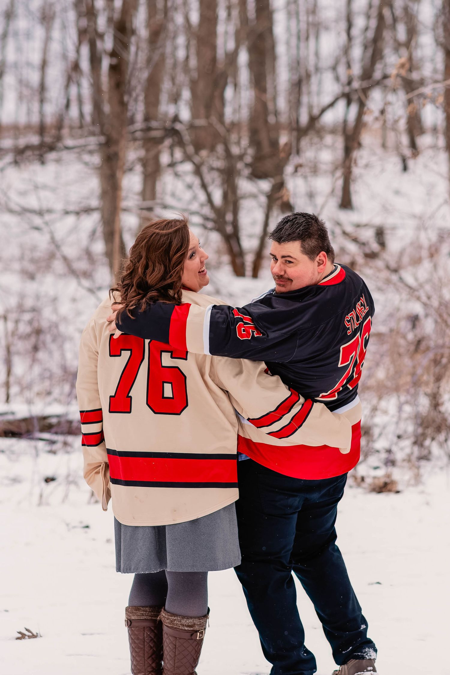 Couple in hockey jerseys embracing in a snowy winter forest setting.
