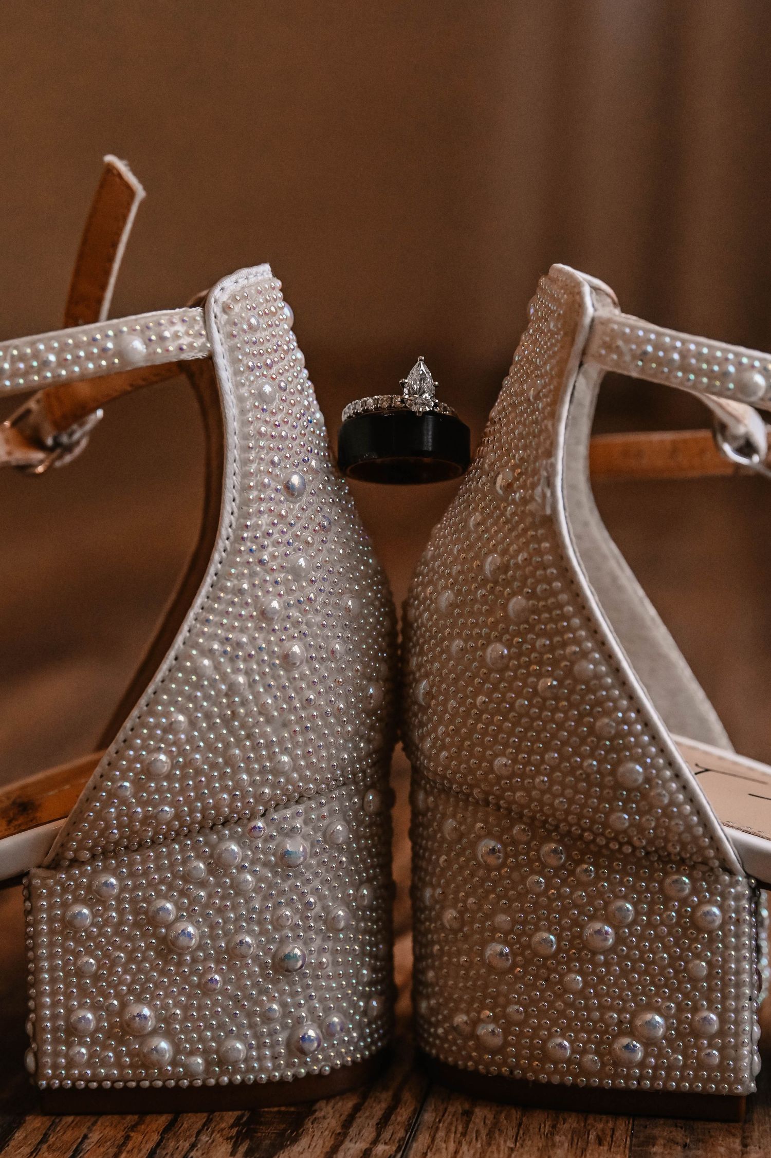 Sparkly rhinestone-encrusted bridal shoes displayed on brown background.