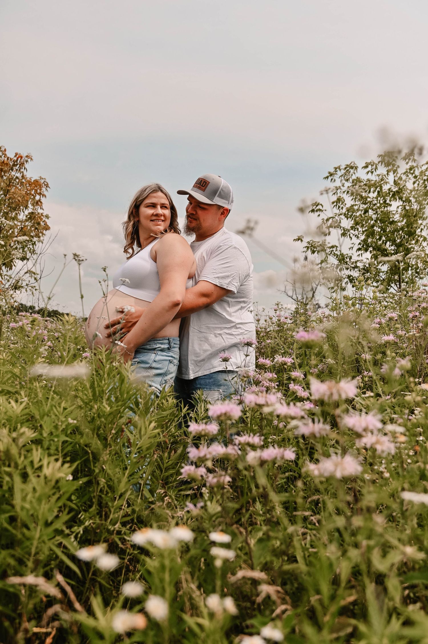 Couple embraces in a field of wildflowers during a romantic outdoor photoshoot at sunset.