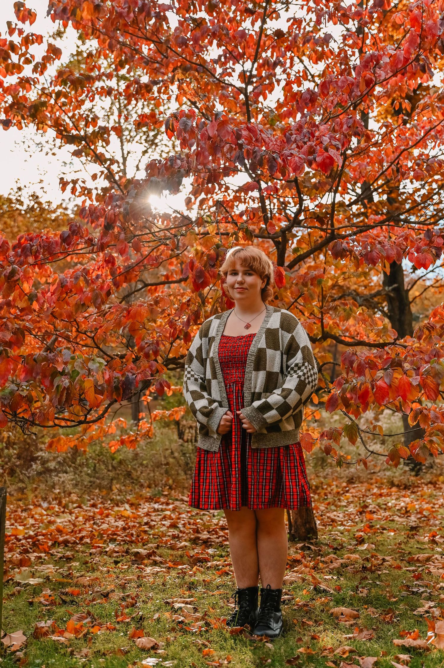 Fall fashion portrait under bright red maple leaves wearing checkered cardigan.