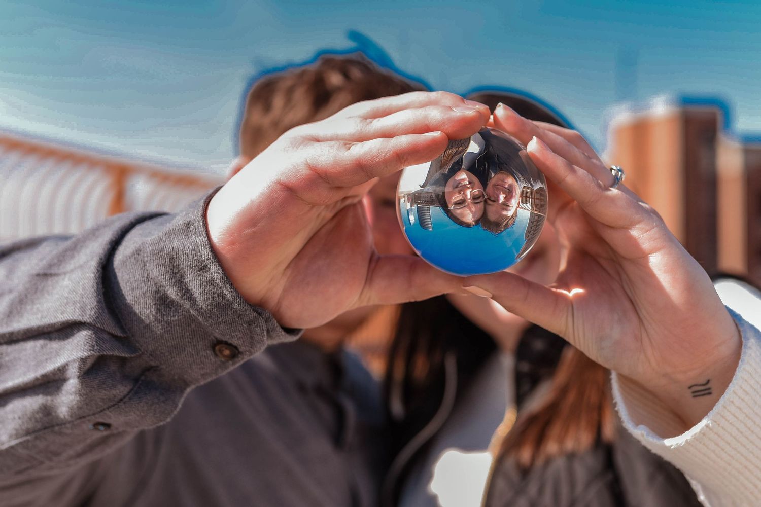 Couple forming a heart shape with their hands against a bright blue sky background.