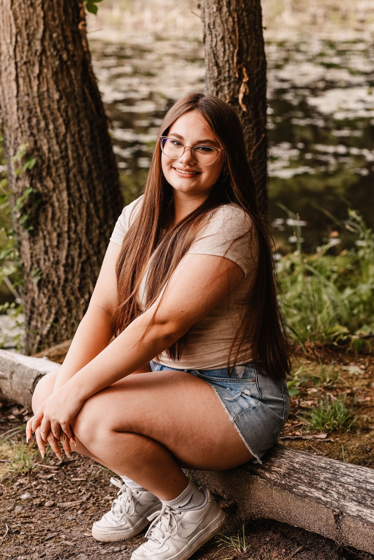 Person sitting casually on log by waterfront in casual summer attire.