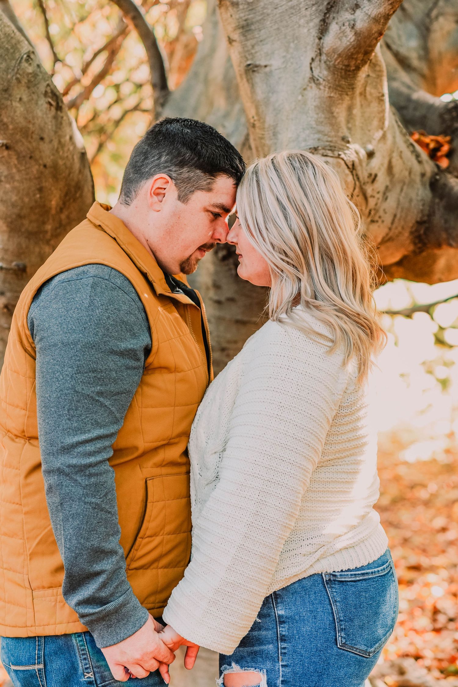 A romantic autumn couple in coordinating outfits share an intimate moment among fall foliage.