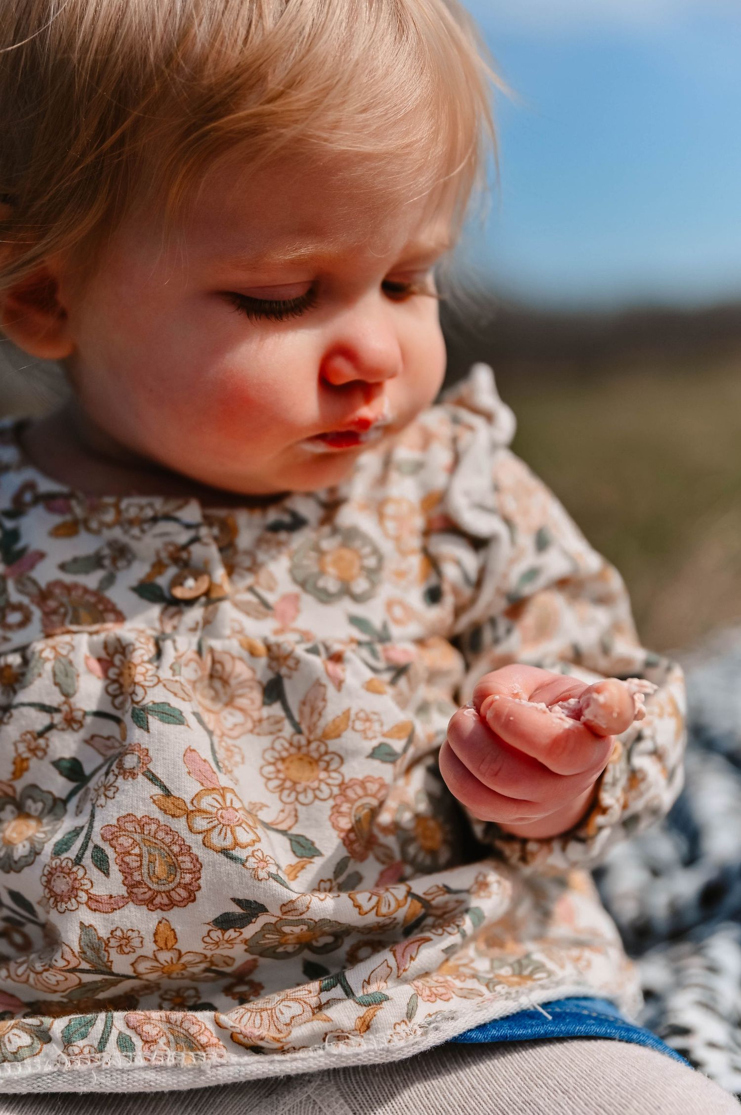 Close-up of baby wearing floral dress lying on patterned blanket outdoors.