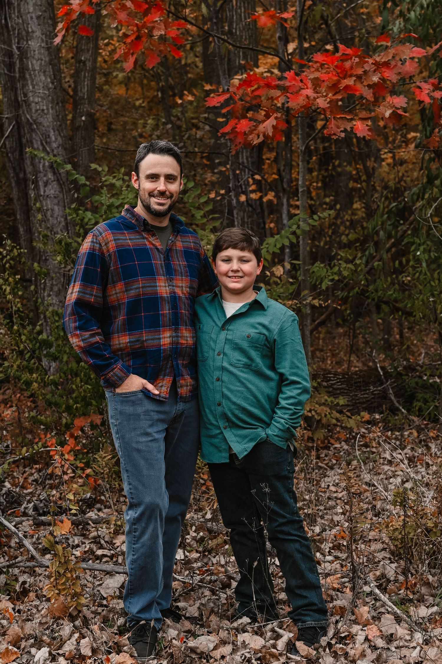 Family standing together against colorful fall foliage in casual attire.