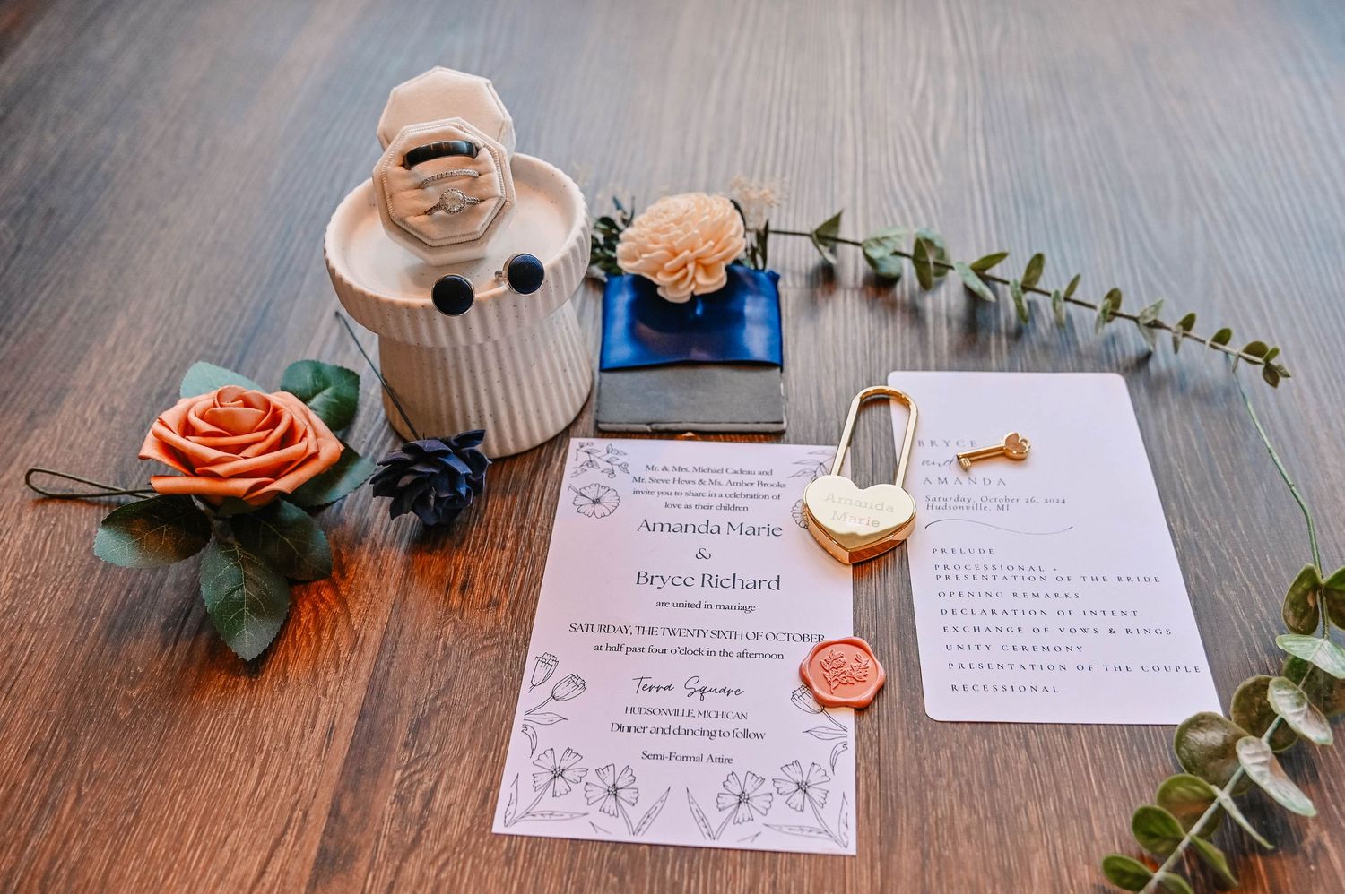 Wedding stationery flatlay with eucalyptus, wax seal, and decorative elements on wooden surface.