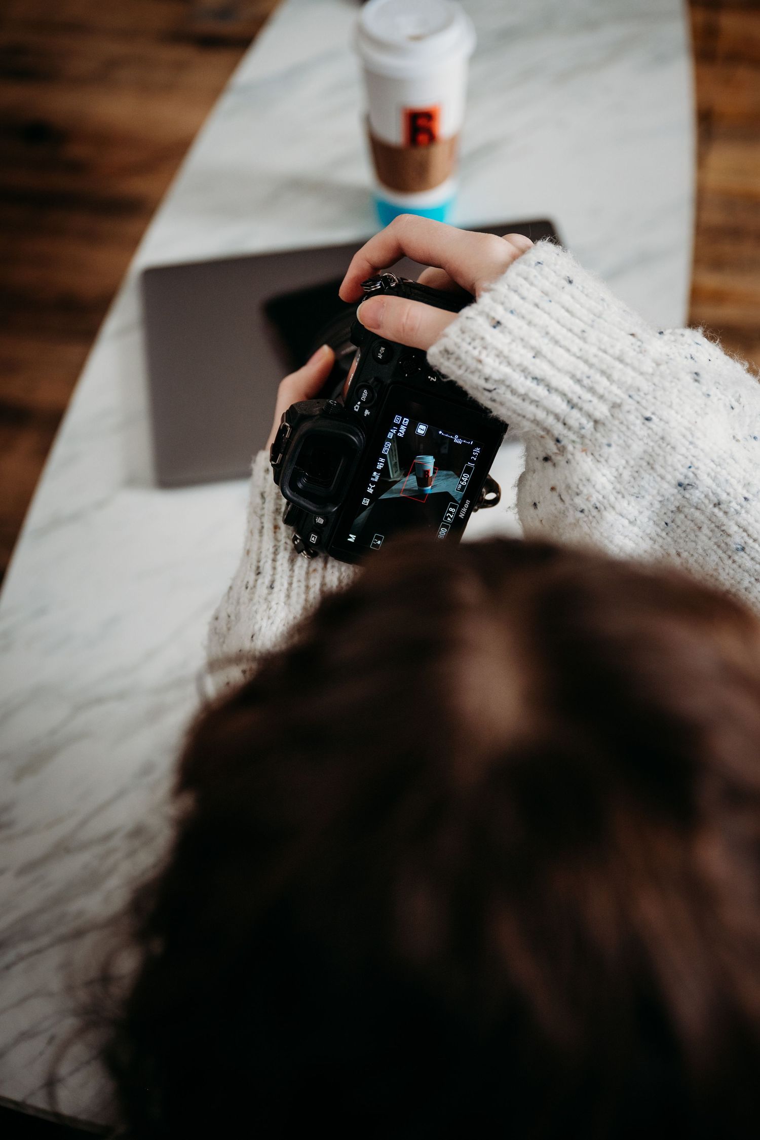 Camera lens cap being held in white sweater sleeve against wooden surface.