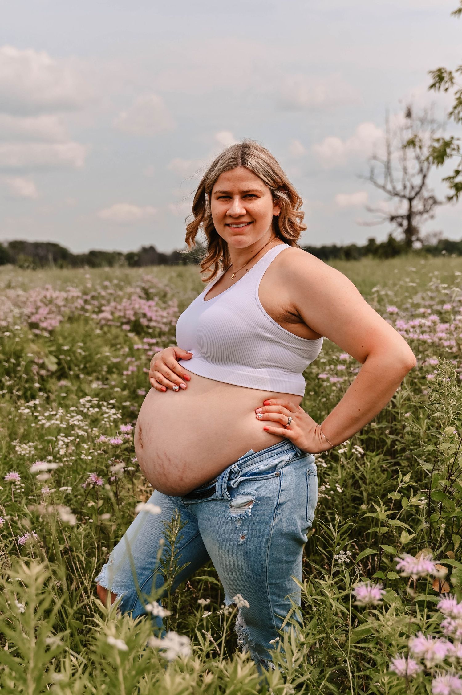 Maternity photoshoot in wildflower field with white tank top and jeans outfit.