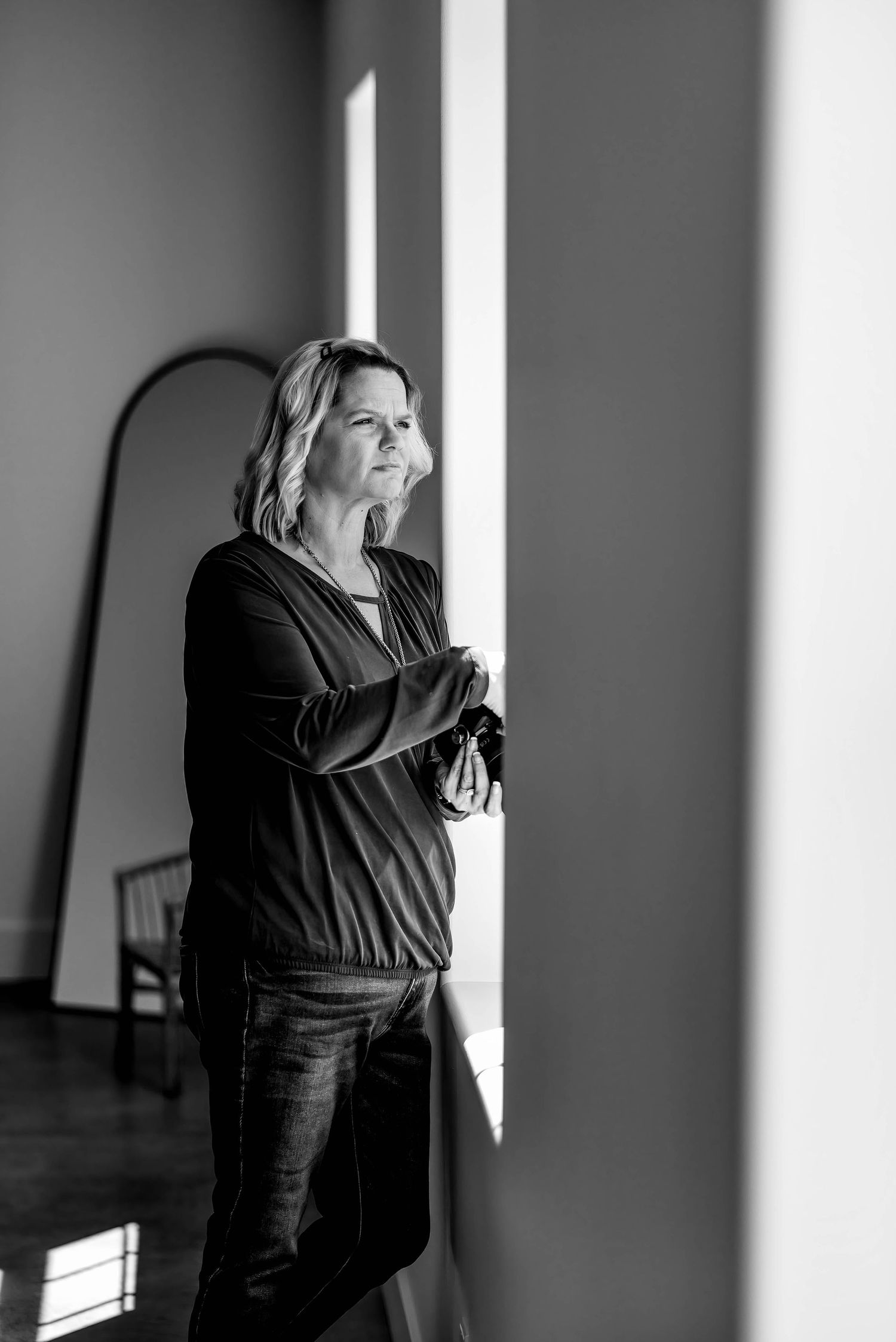 Black and white portrait of person standing in dramatic window light.