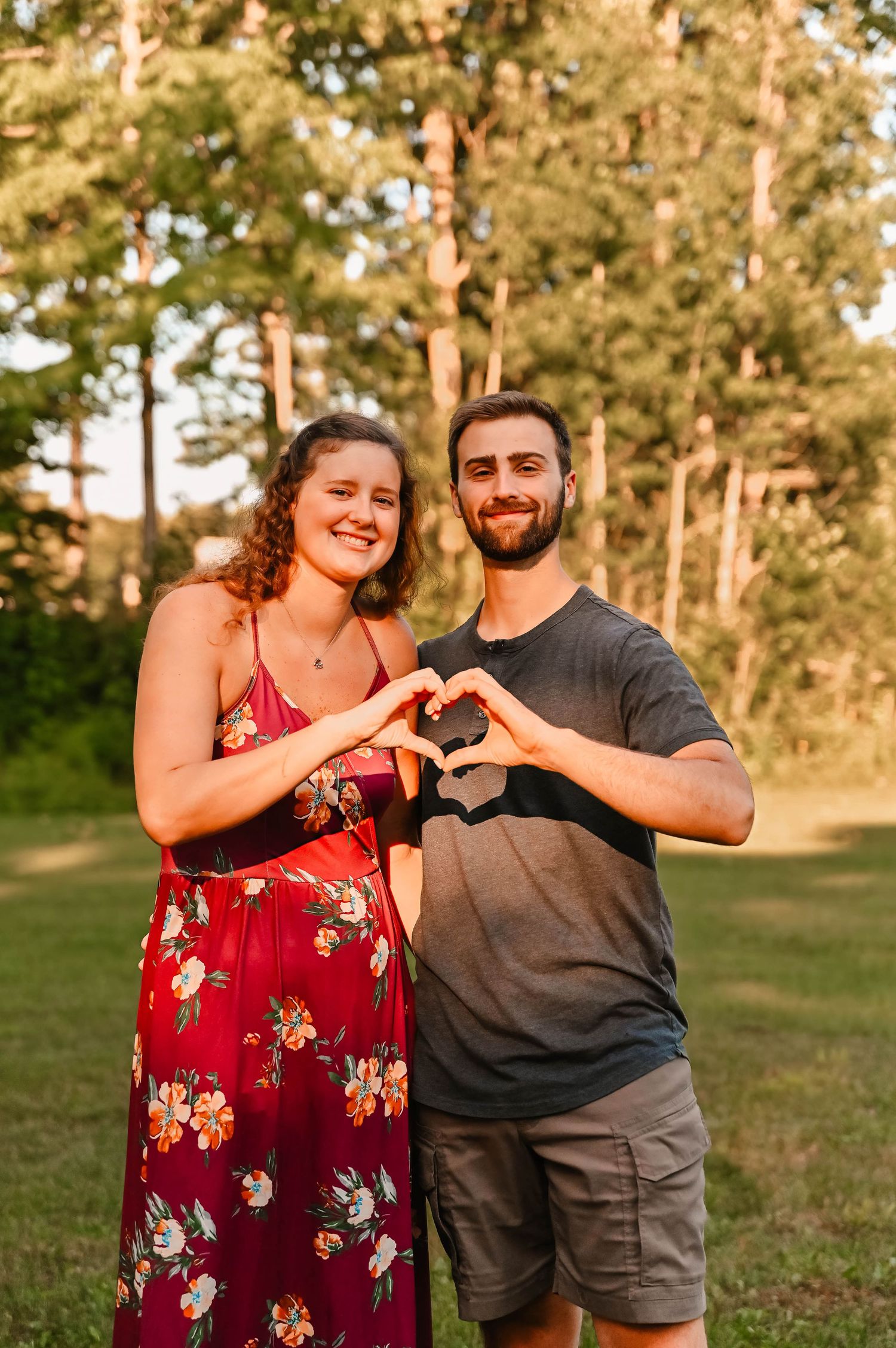 Couple making heart shape with hands in outdoor setting.