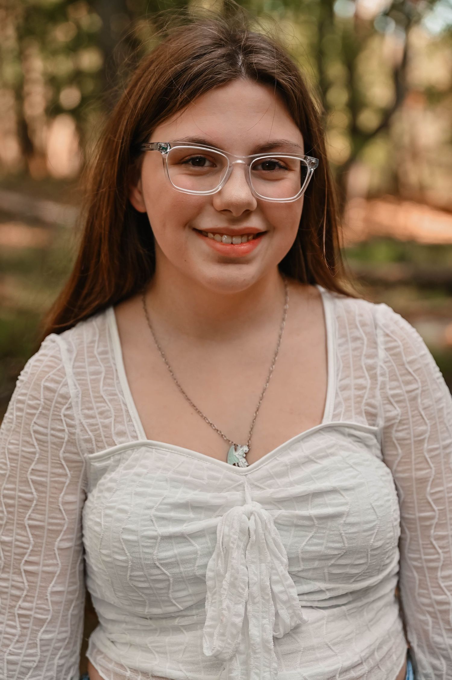 Close-up portrait wearing white textured top and glasses with natural woodland backdrop.