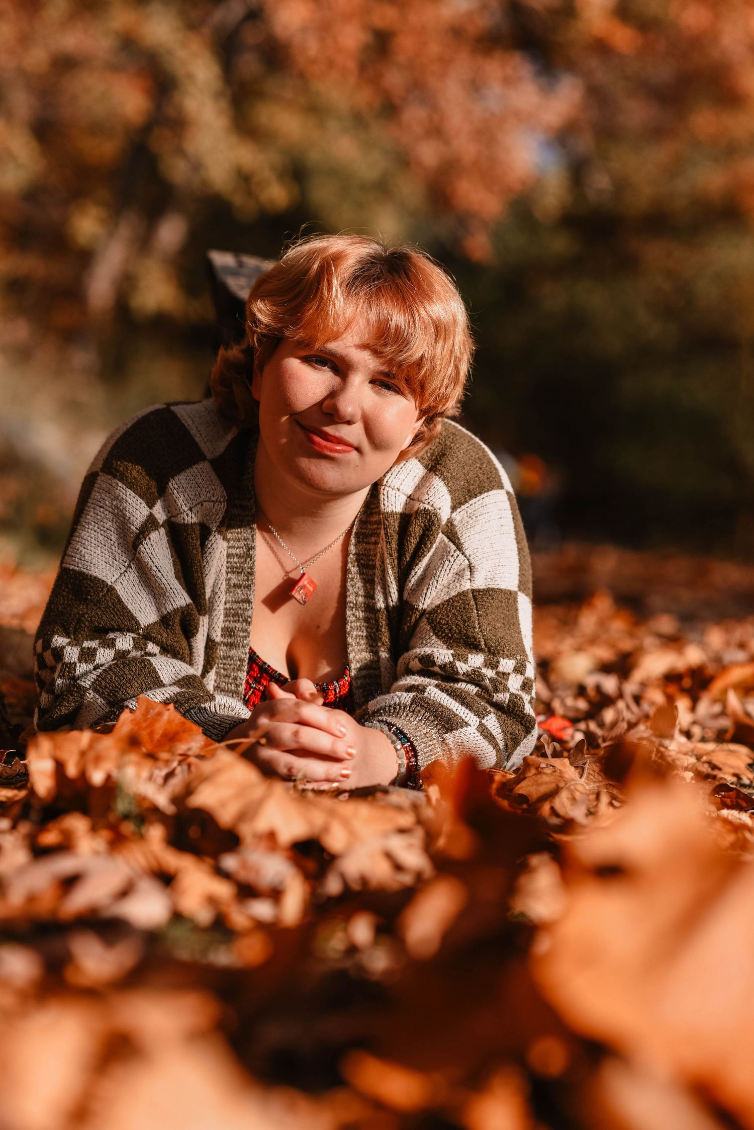 Autumn portrait in cozy sweater lying among orange fallen leaves.