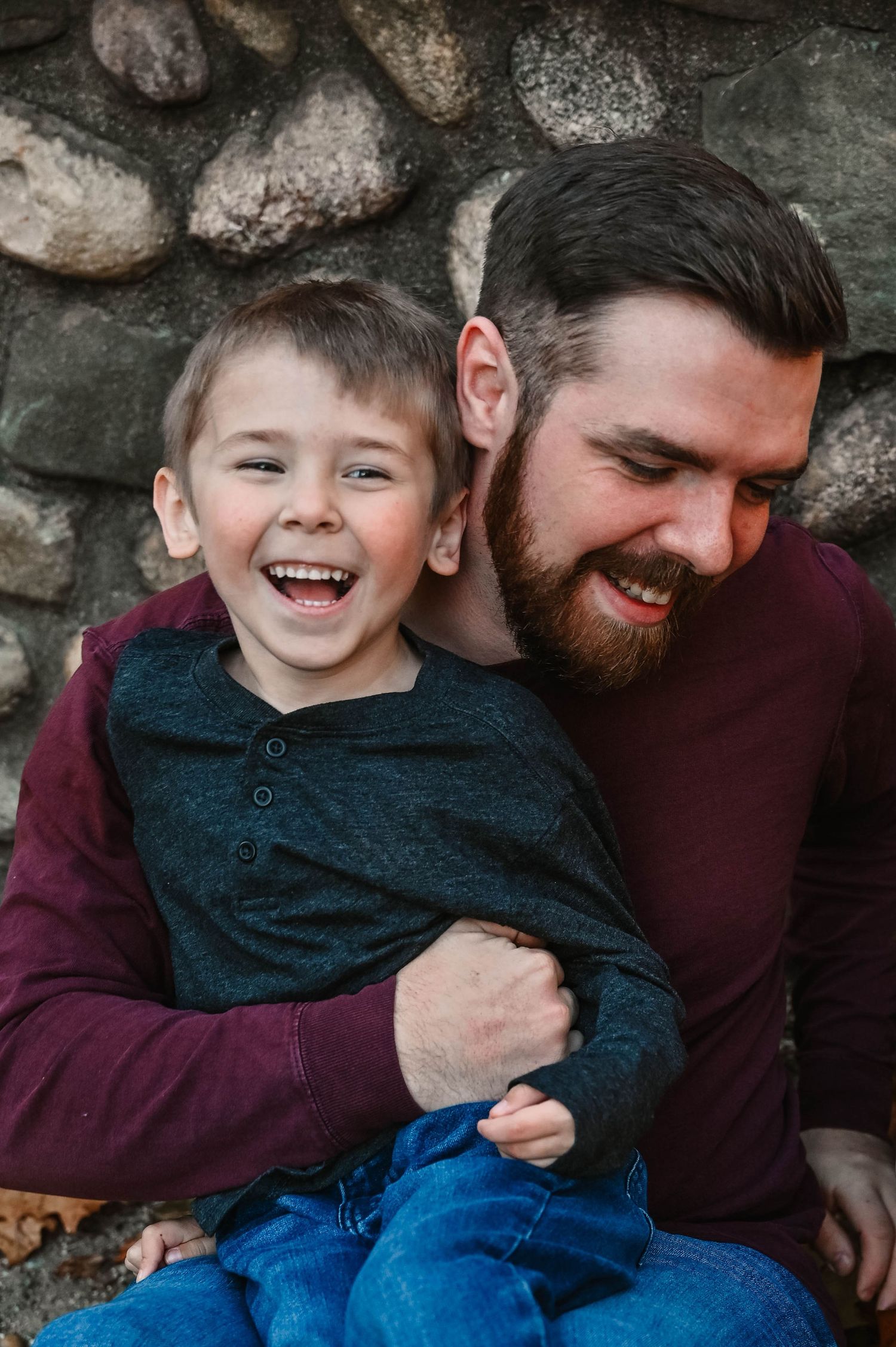 Heartwarming moment between parent and child laughing against a rustic stone wall.