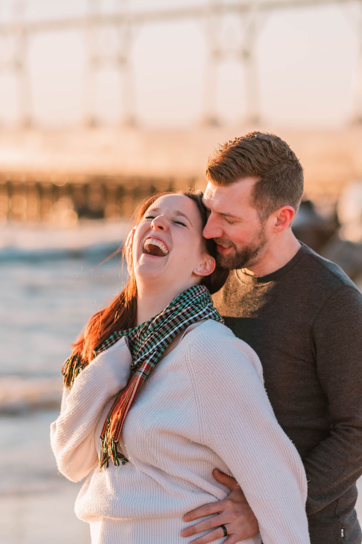 Joyful couple sharing laughter during sunset beach photoshoot.