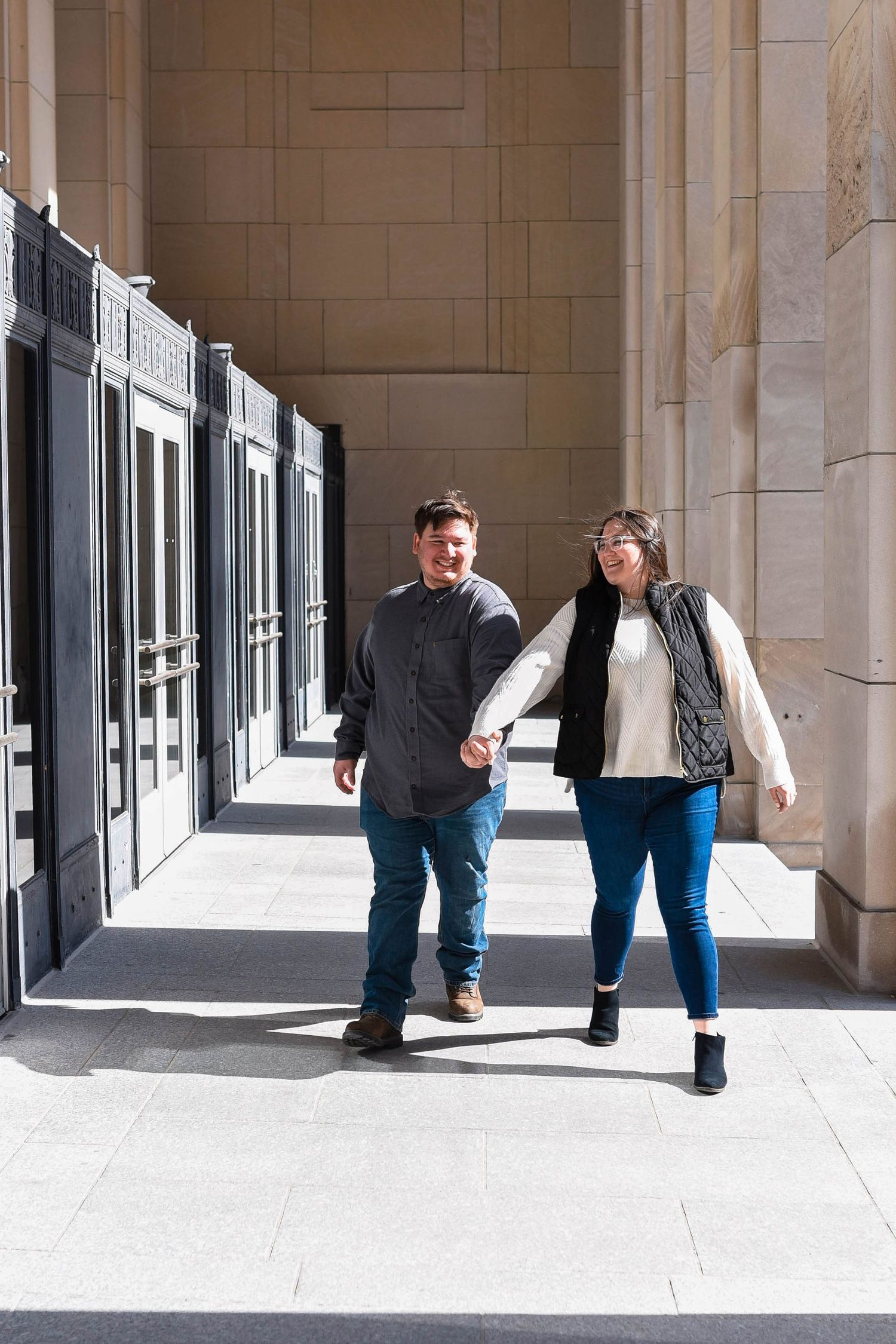 A couple sharing playful moments in a colonnade with dramatic lighting and shadows.