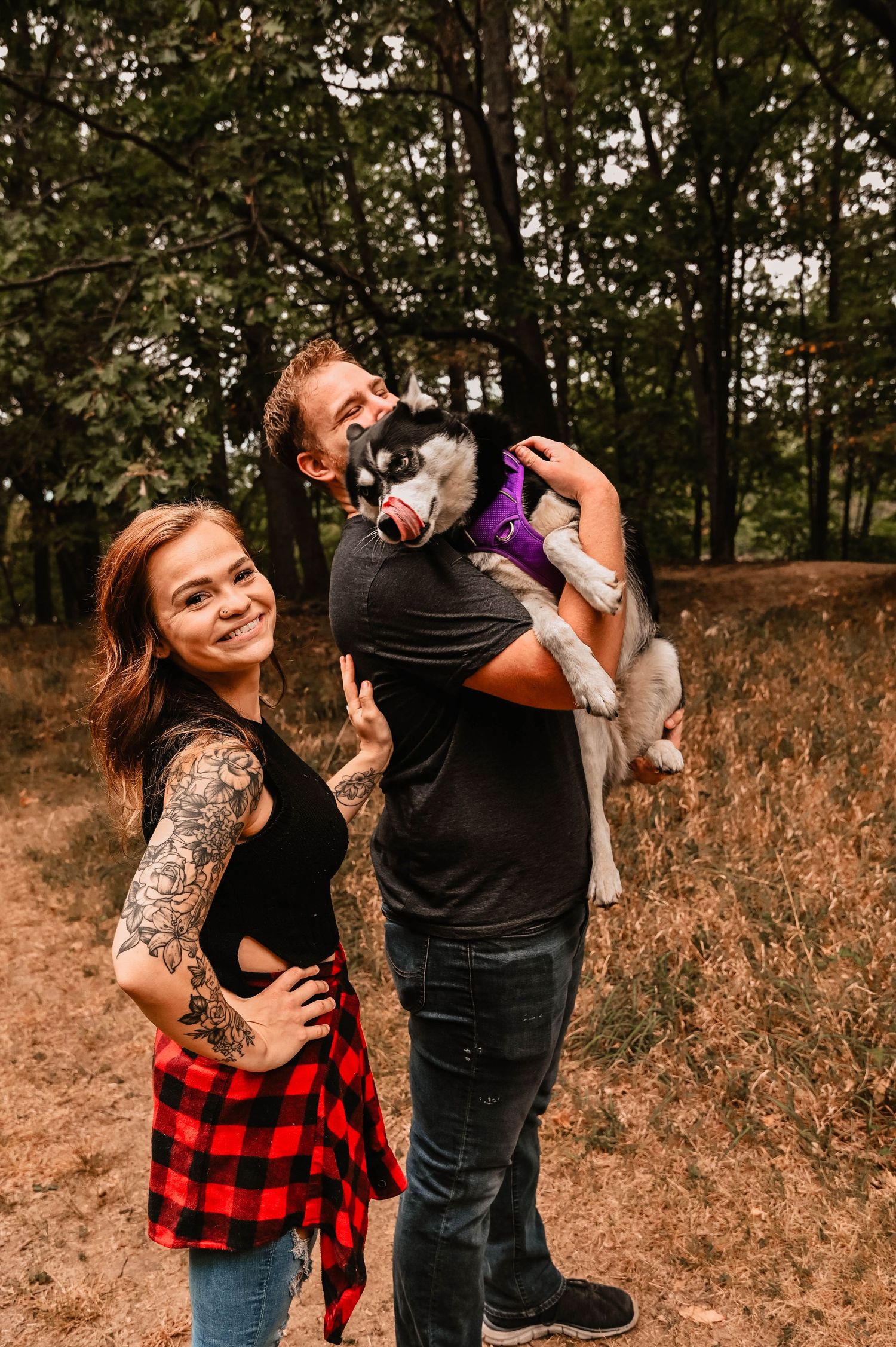 A couple dancing and playing with their dog in a rustic outdoor setting.