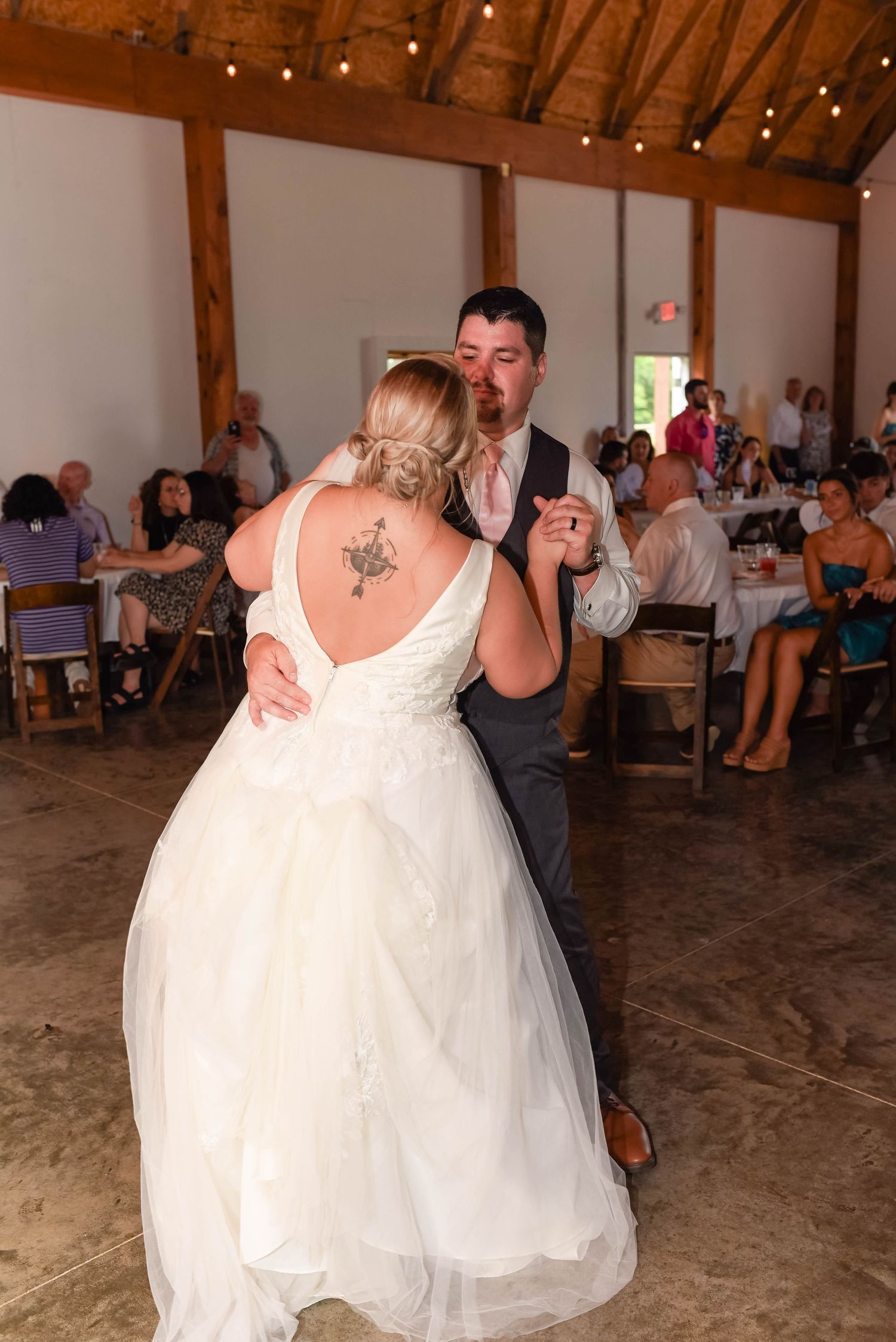 A couple shares their first dance in a rustic barn venue decorated with string lights.