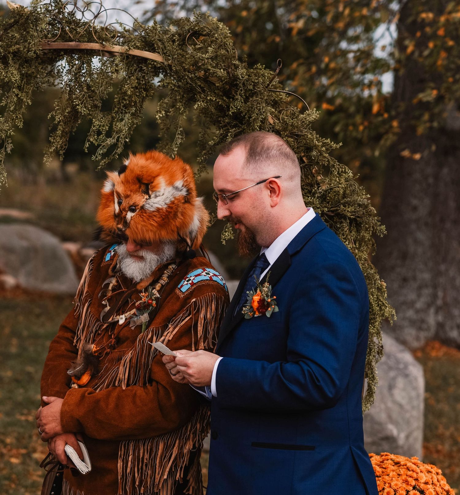 Wedding ceremony outdoors with rustic fall decorations and orange accents.