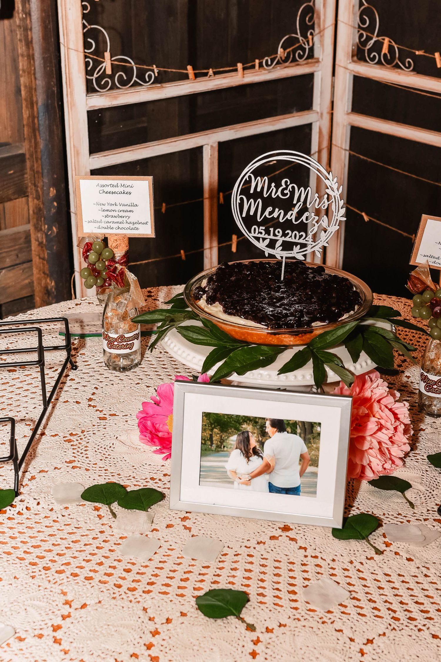 Wedding reception table with lace tablecloth, decorative signs and floral arrangements.