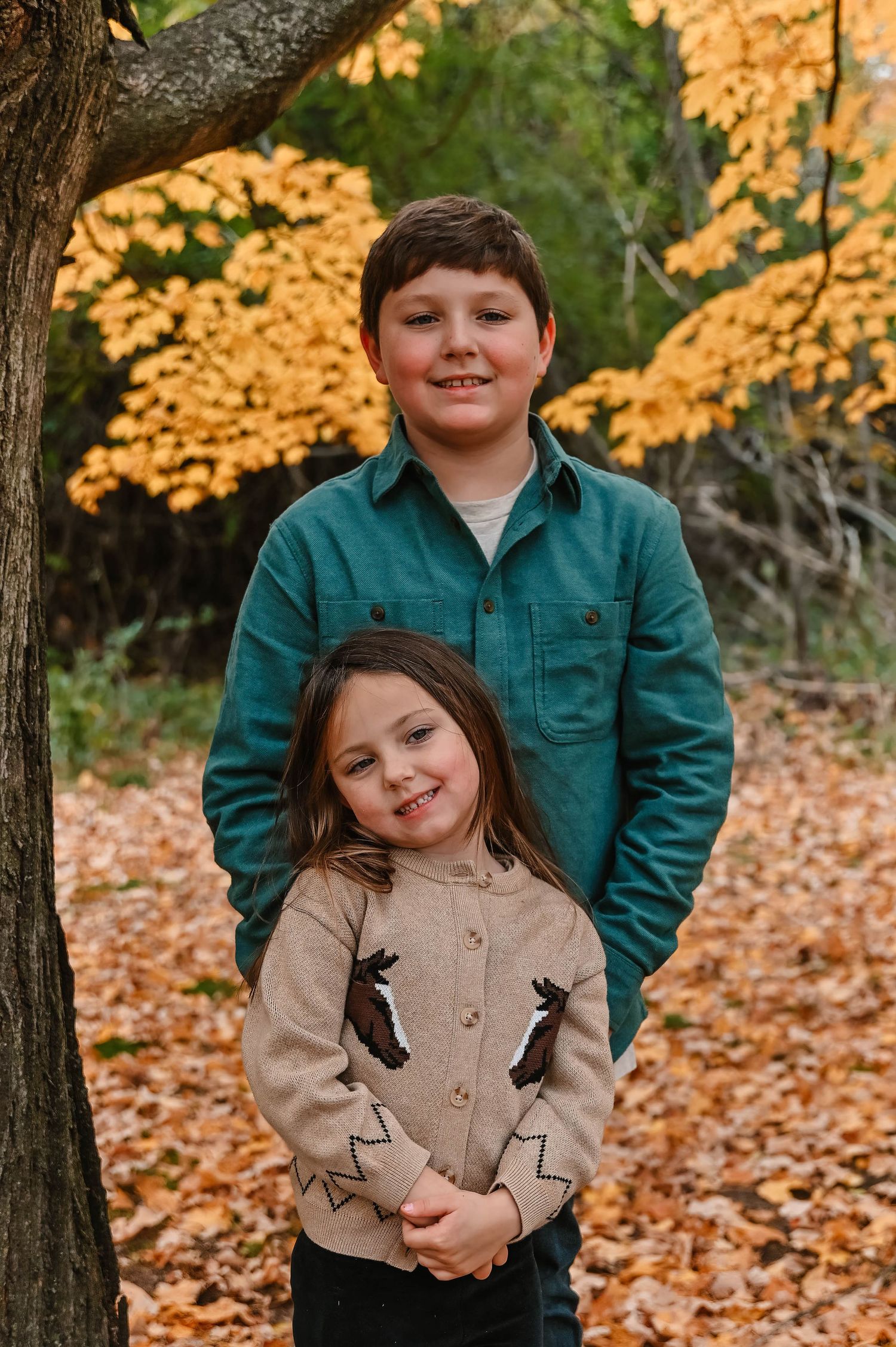 Two kids sharing a playful moment together in a fall forest setting.