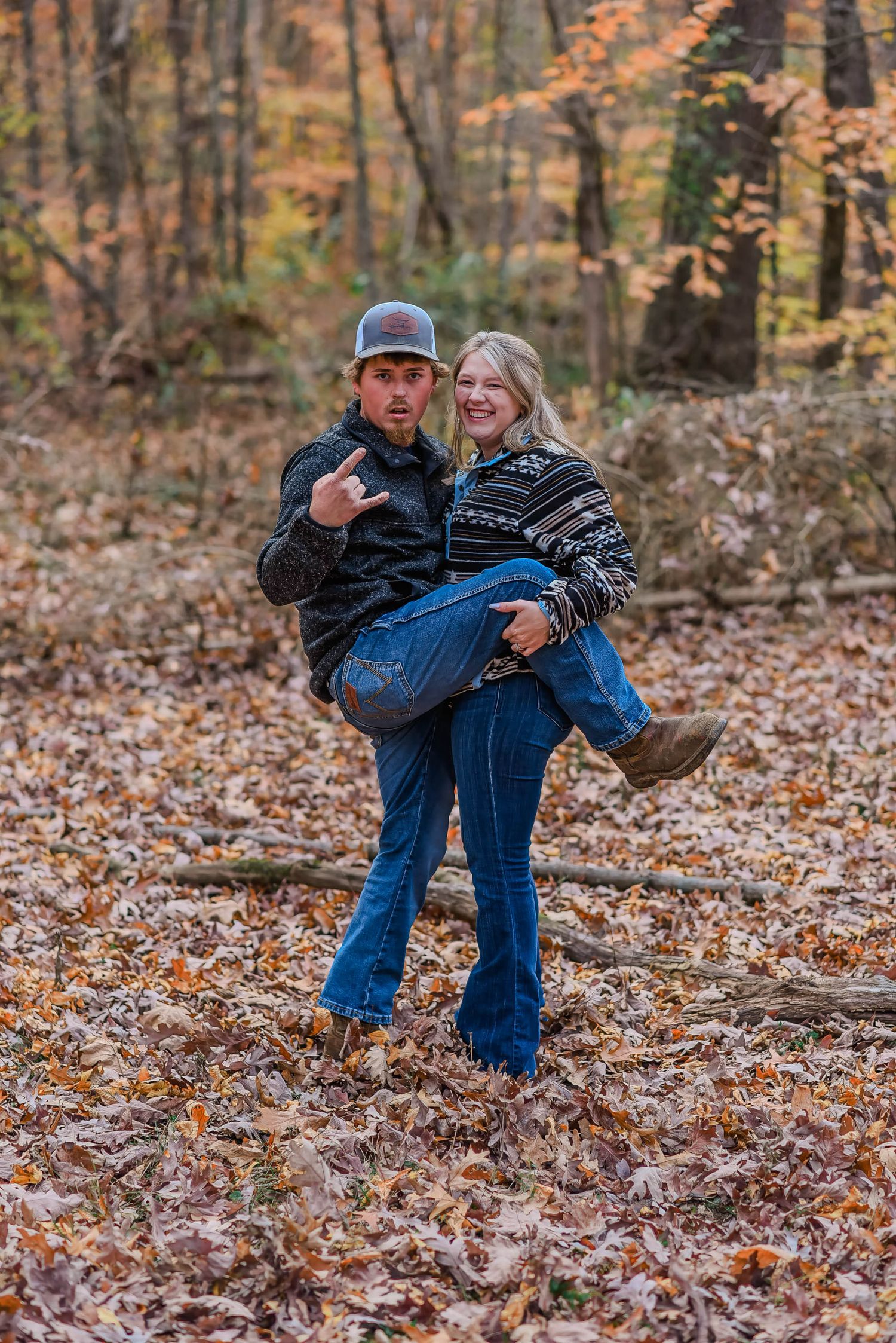 Couple playing and dancing in fallen autumn leaves during outdoor photoshoot.