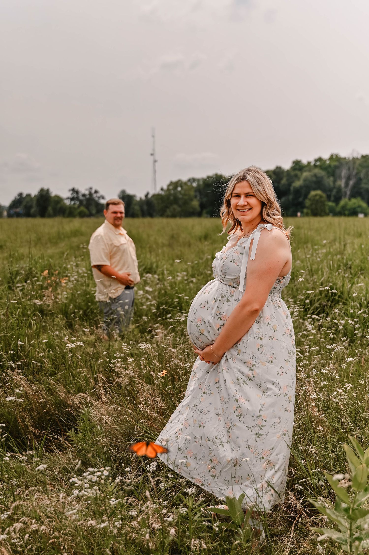 A couple poses in a wildflower meadow for engagement photos with a tower visible in the background.