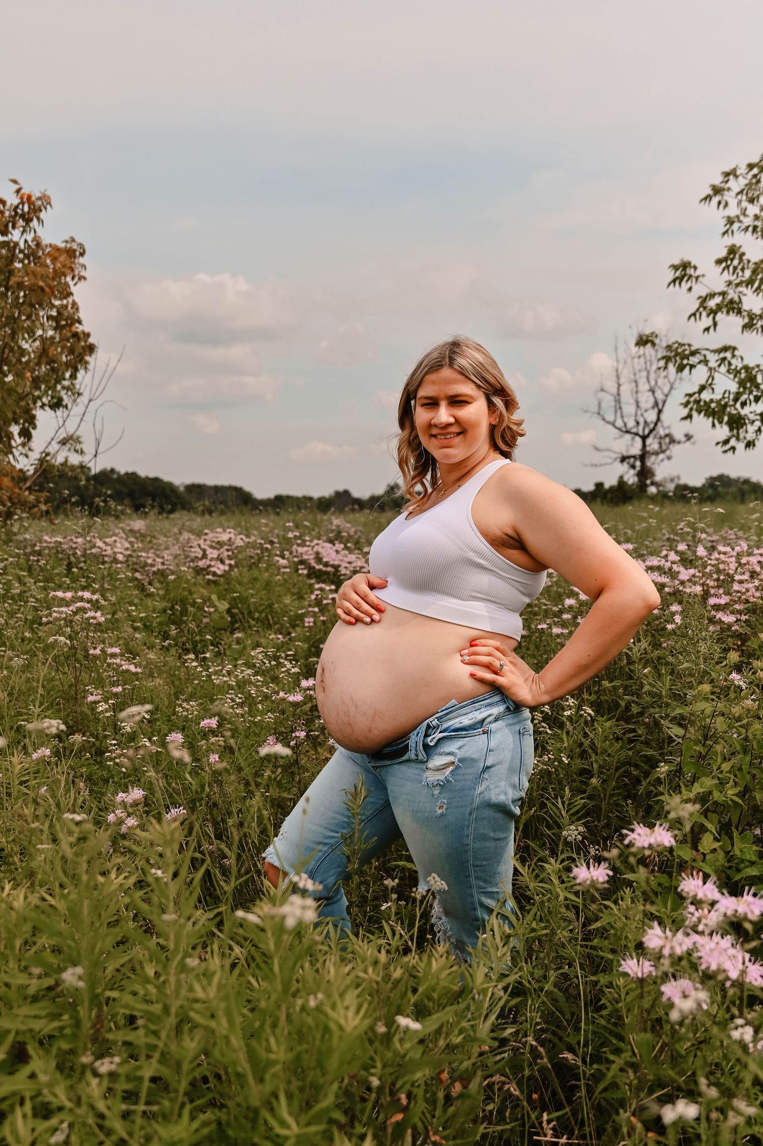 A maternity session captures candid moments in a field of pink wildflowers during golden hour.