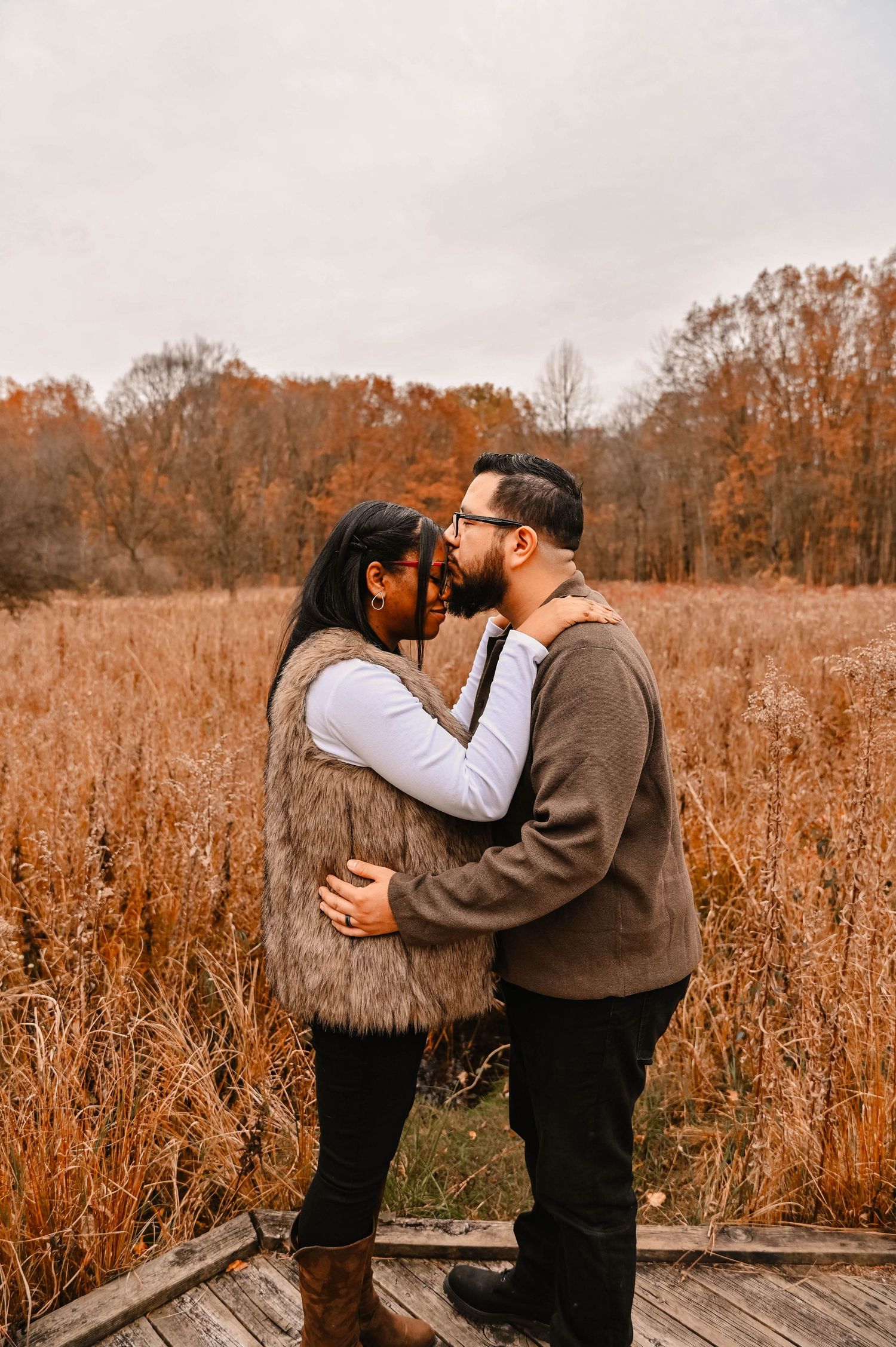 A romantic autumn photoshoot shows tender moments between a couple on a wooden boardwalk.