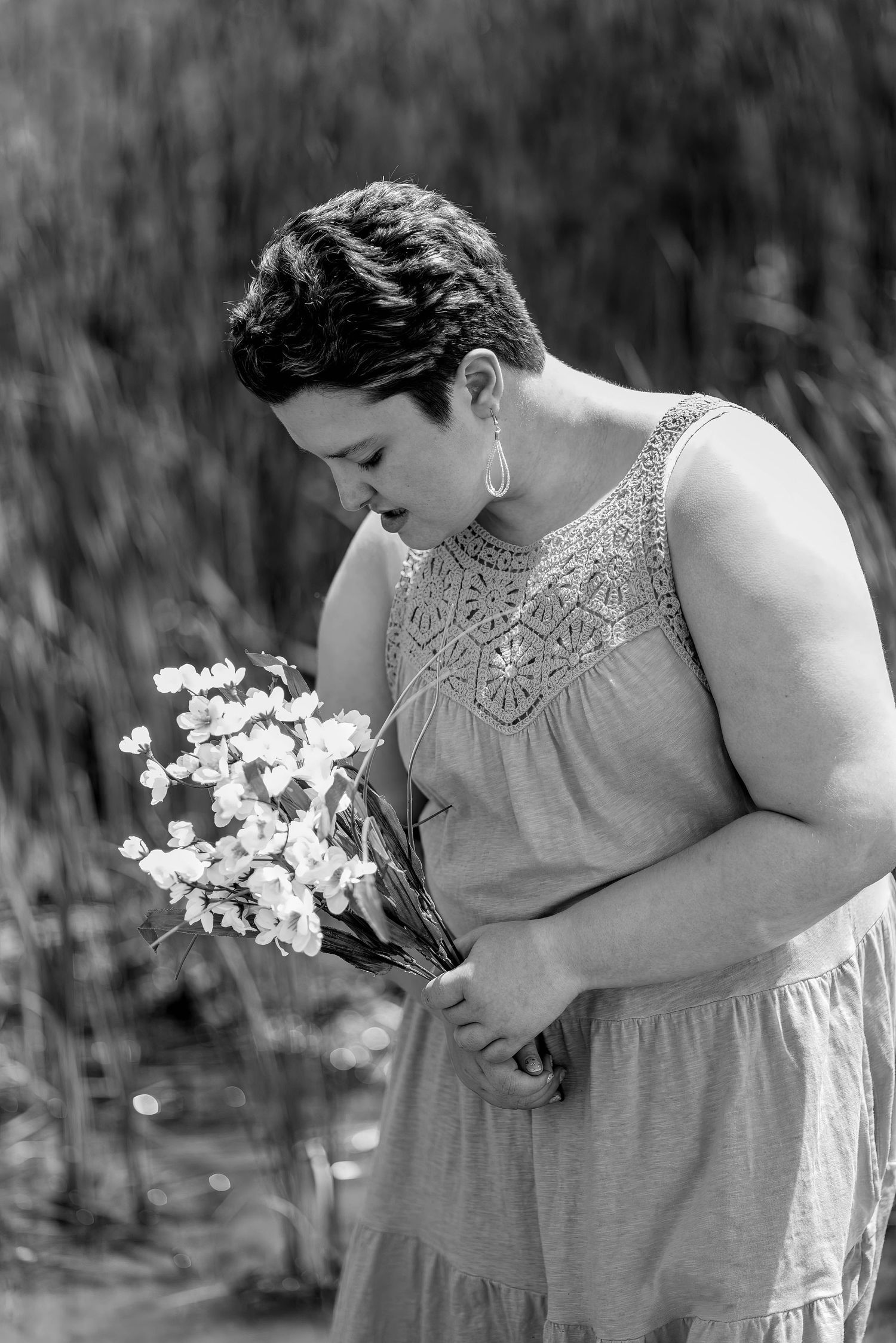 A person in a lace dress looks down at white flowers in a black and white portrait.