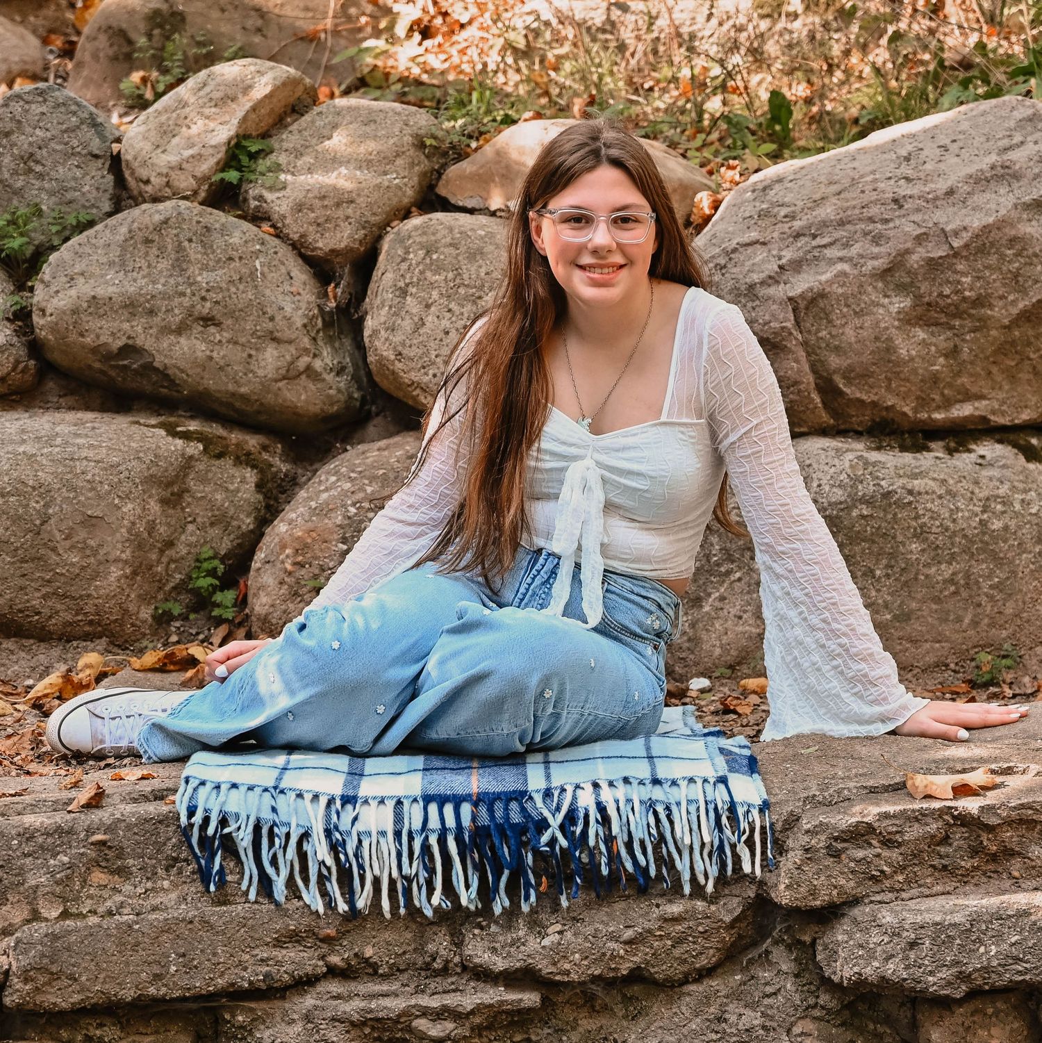 Someone in casual attire lounges on a rustic stone wall surrounded by autumn foliage.