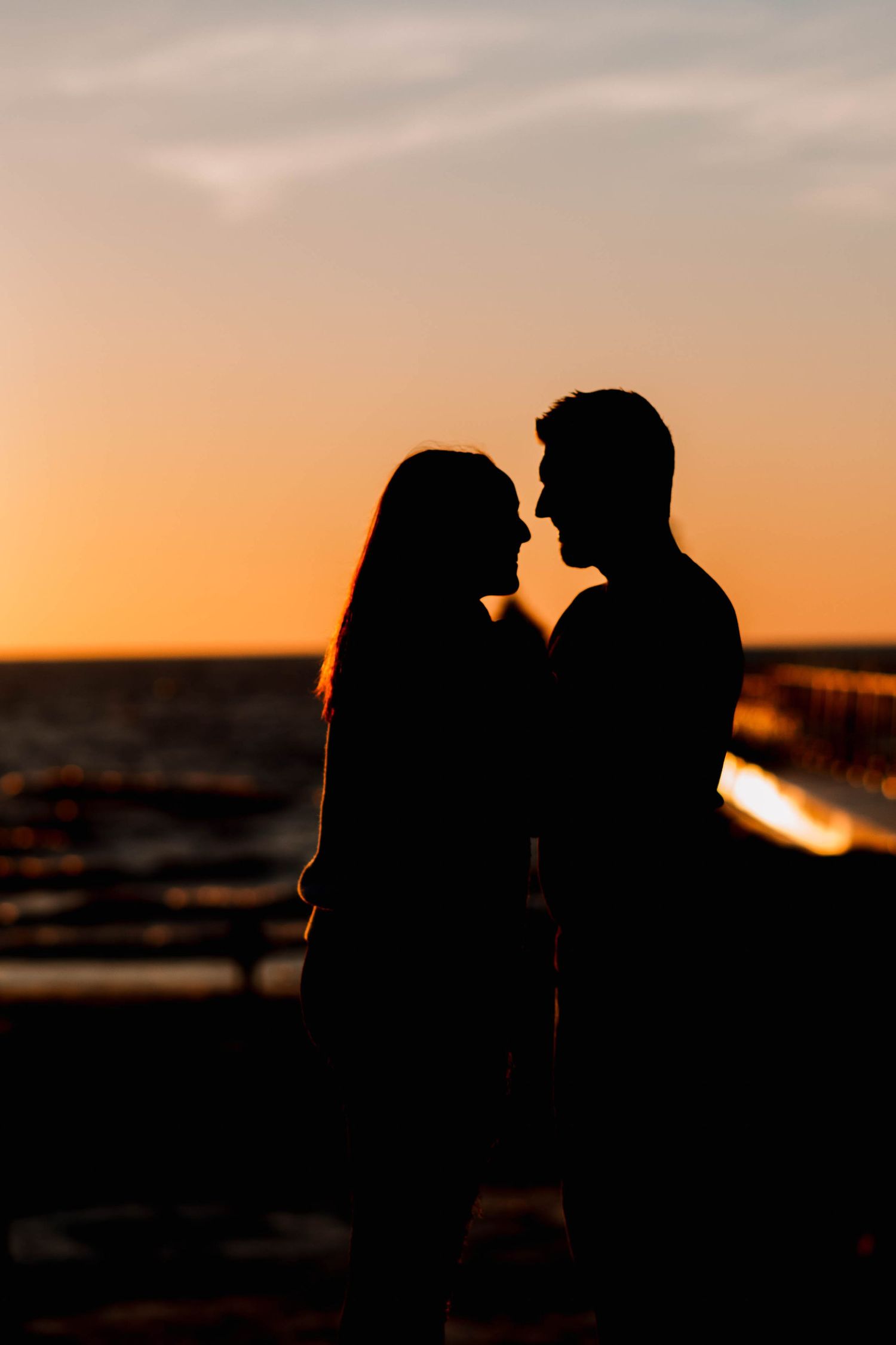 Silhouettes of a couple in romantic poses against a dramatic sunset beach backdrop.