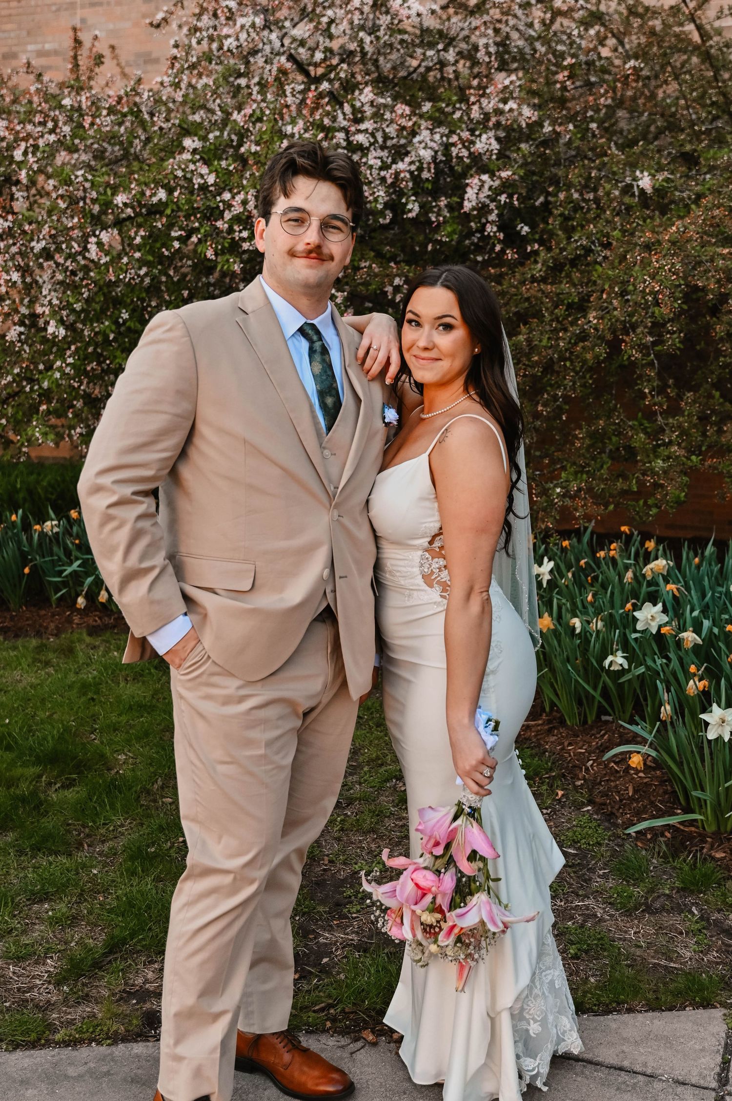 Wedding couple poses in front of flowering bush in spring garden setting.