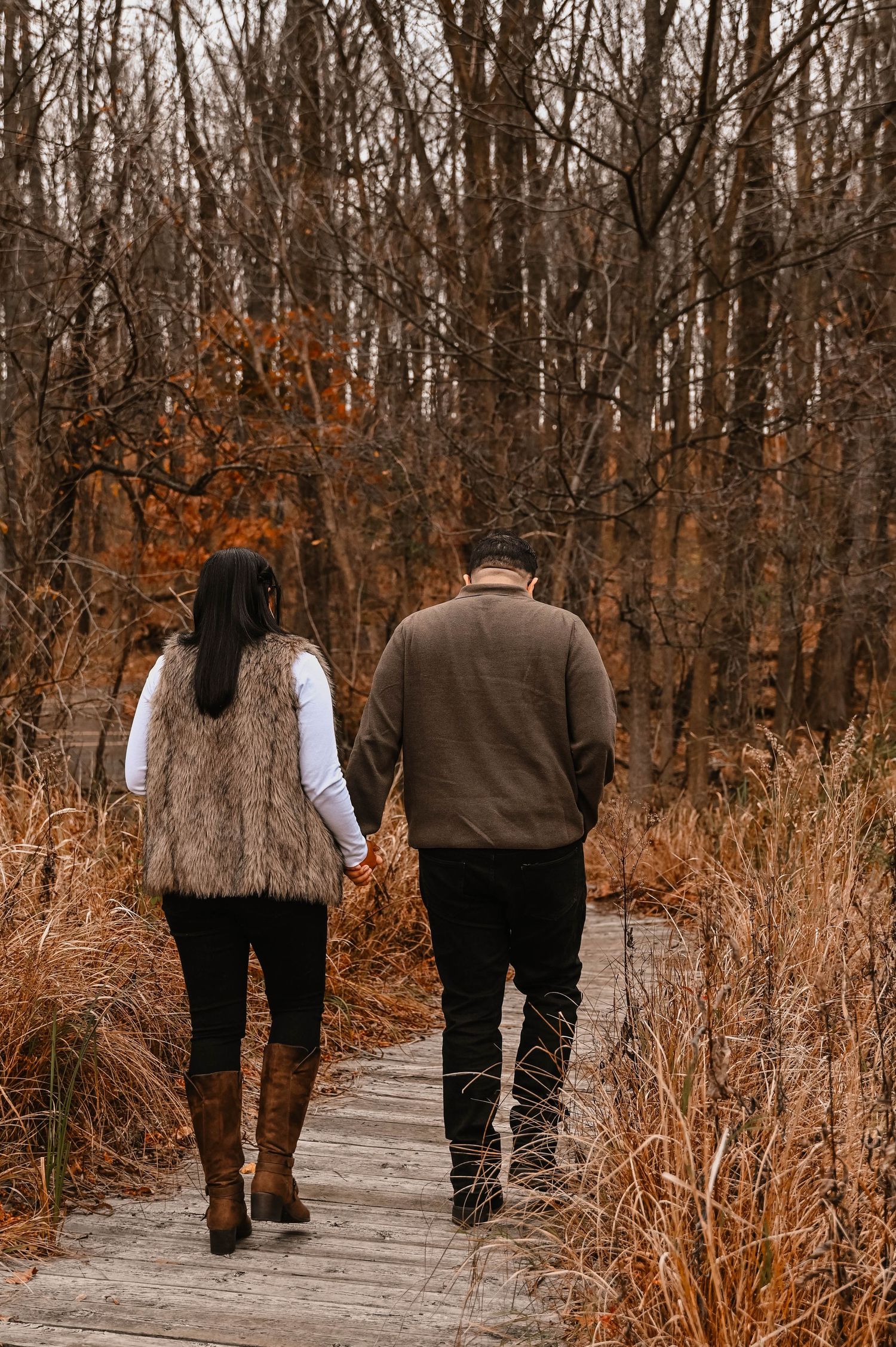 A couple walks hand in hand through a path surrounded by autumn trees.