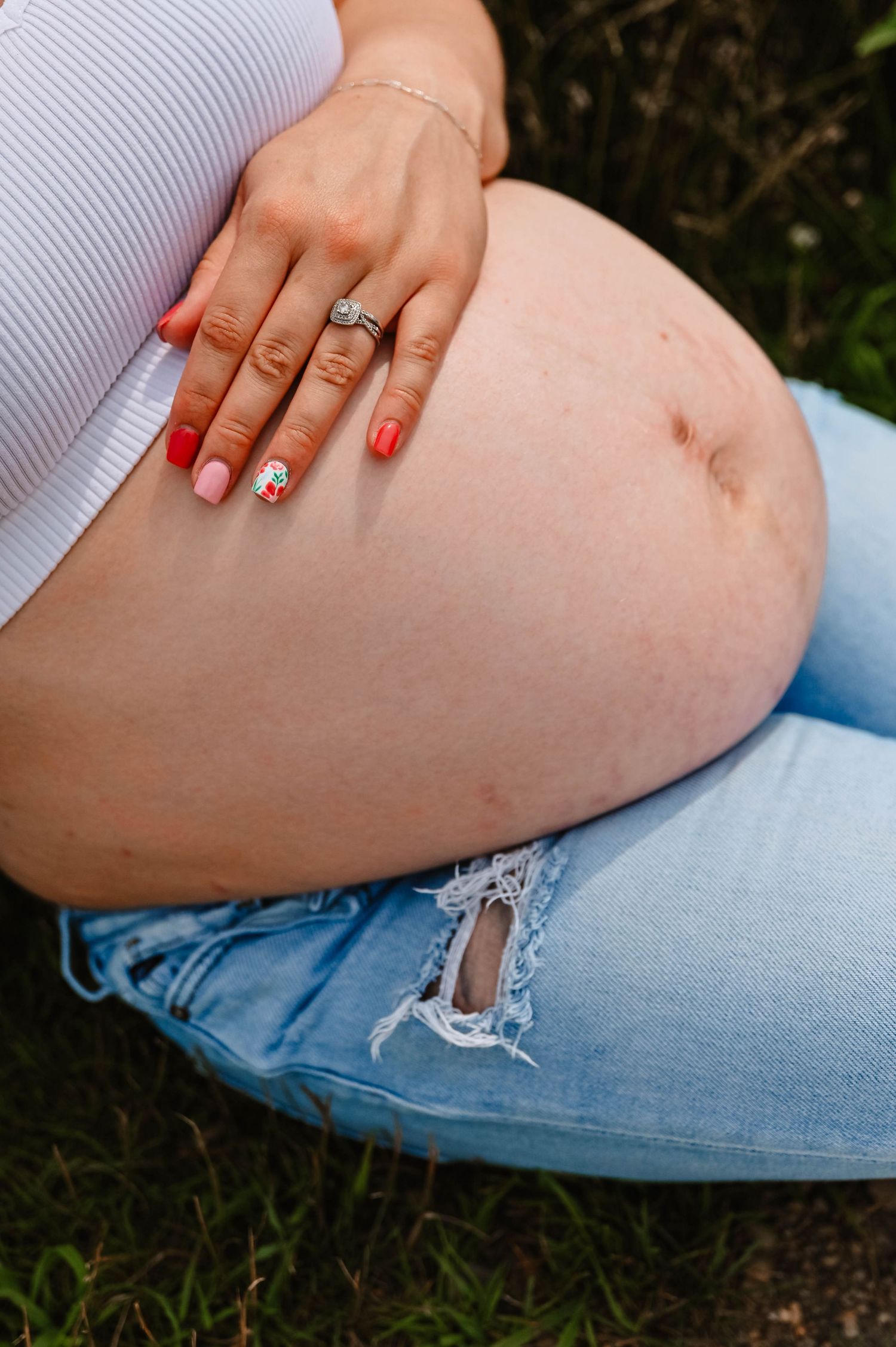 Detail shots of hands with red nails resting on a pregnant belly with distressed denim jeans.