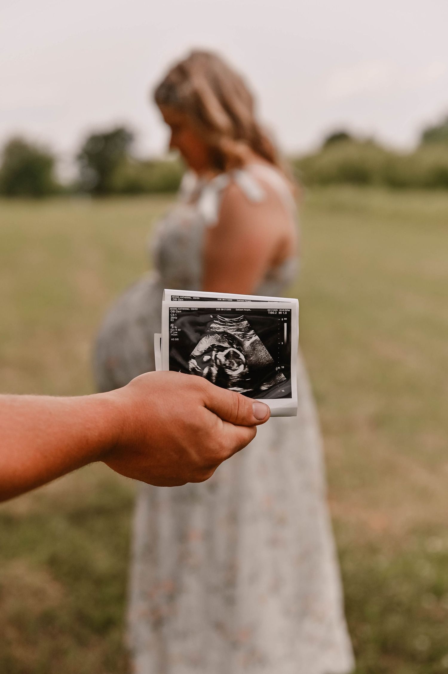 Hands holding up black and white ultrasound images in a sunny field.