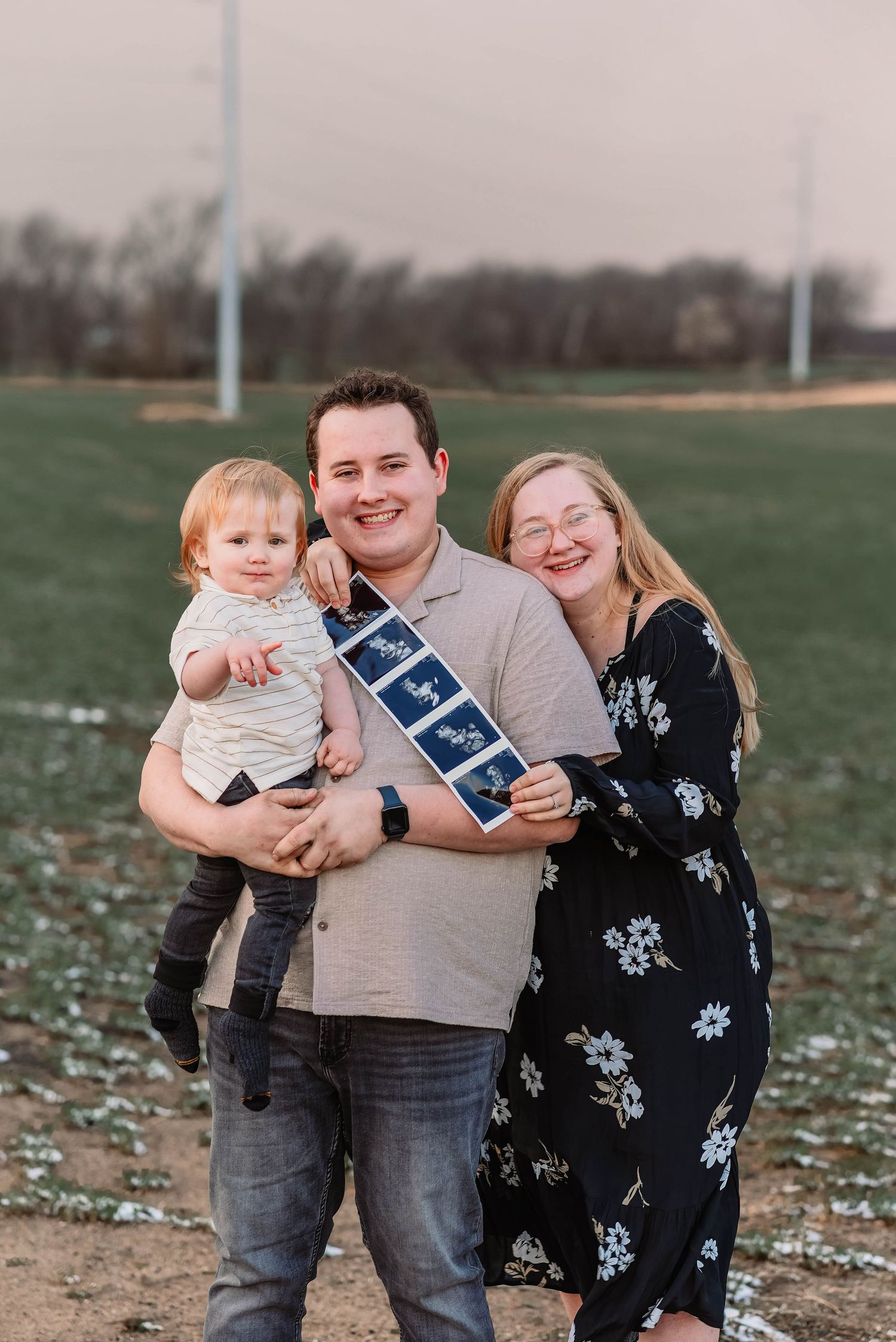 A family poses together on a field holding a blue banner for a pregnancy announcement photo.