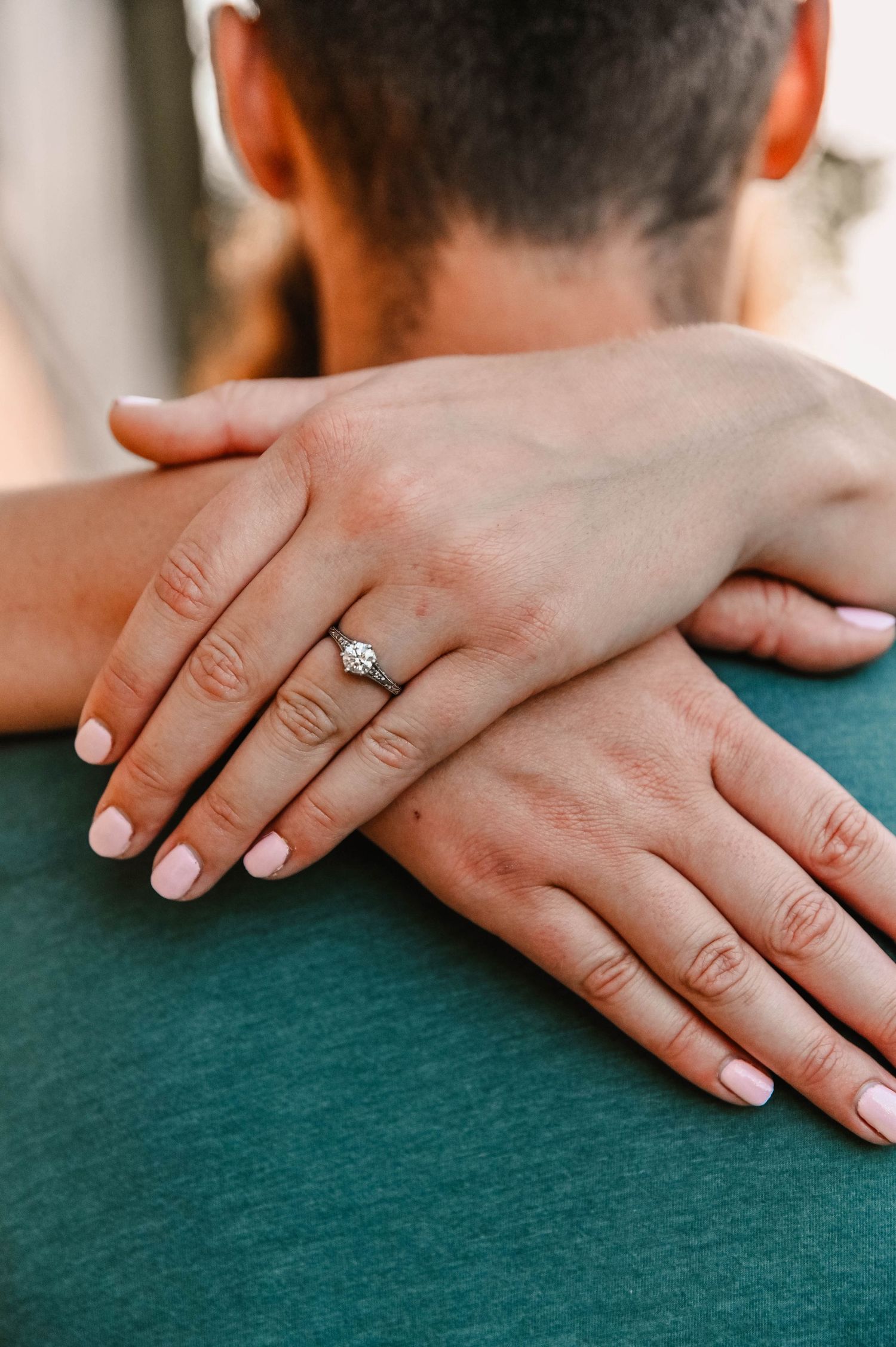 A close-up shot of hands with minimal jewelry resting on a dark teal textured fabric surface.