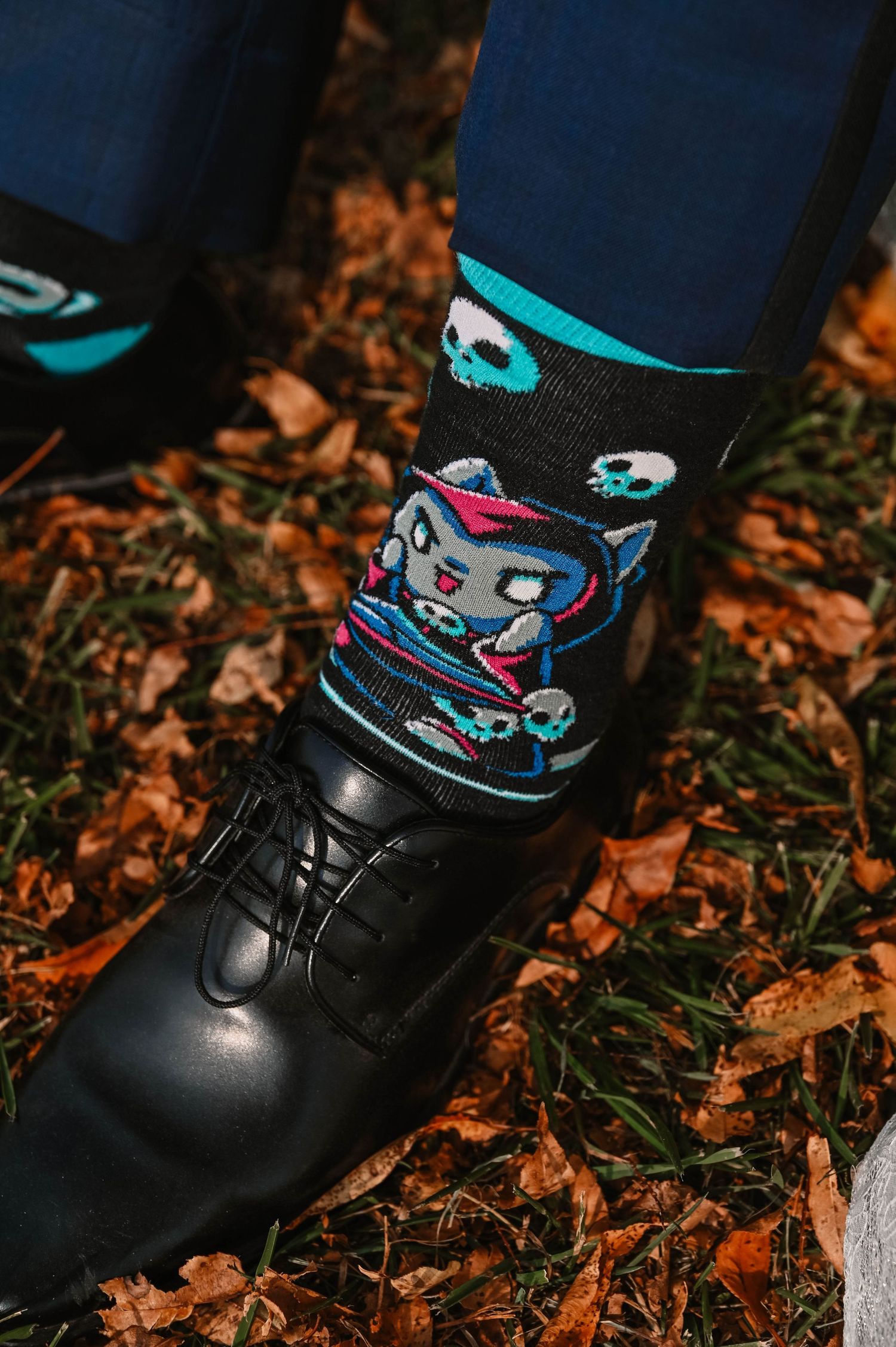 Black dress shoes with colorful patterned socks on fallen autumn leaves.