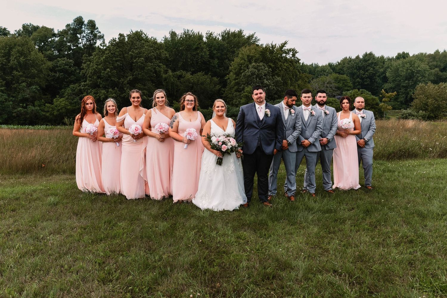Wedding party poses for formal group photo outdoors with bridesmaids in pink dresses.
