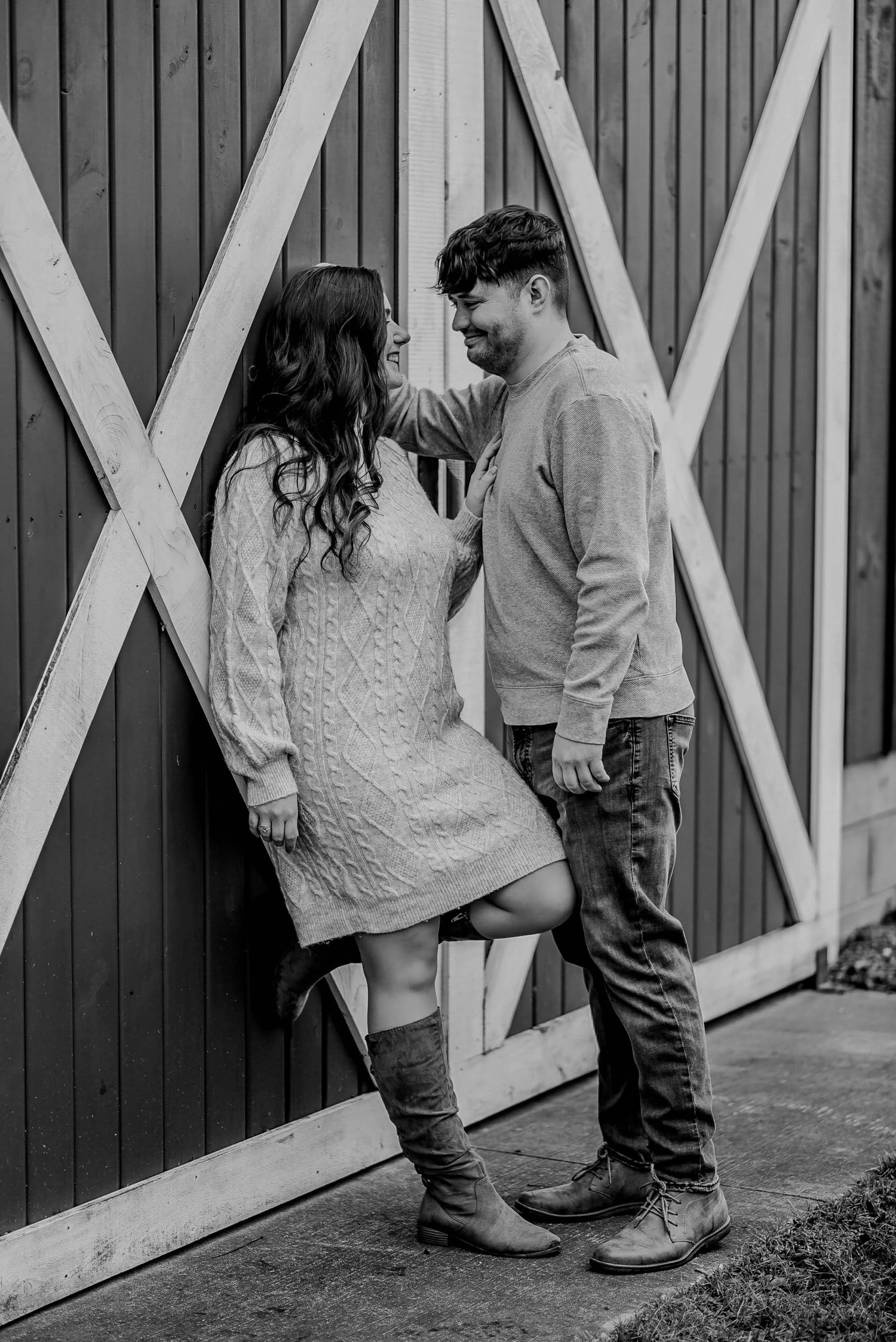 Black and white view of couple standing against rustic barn doors.