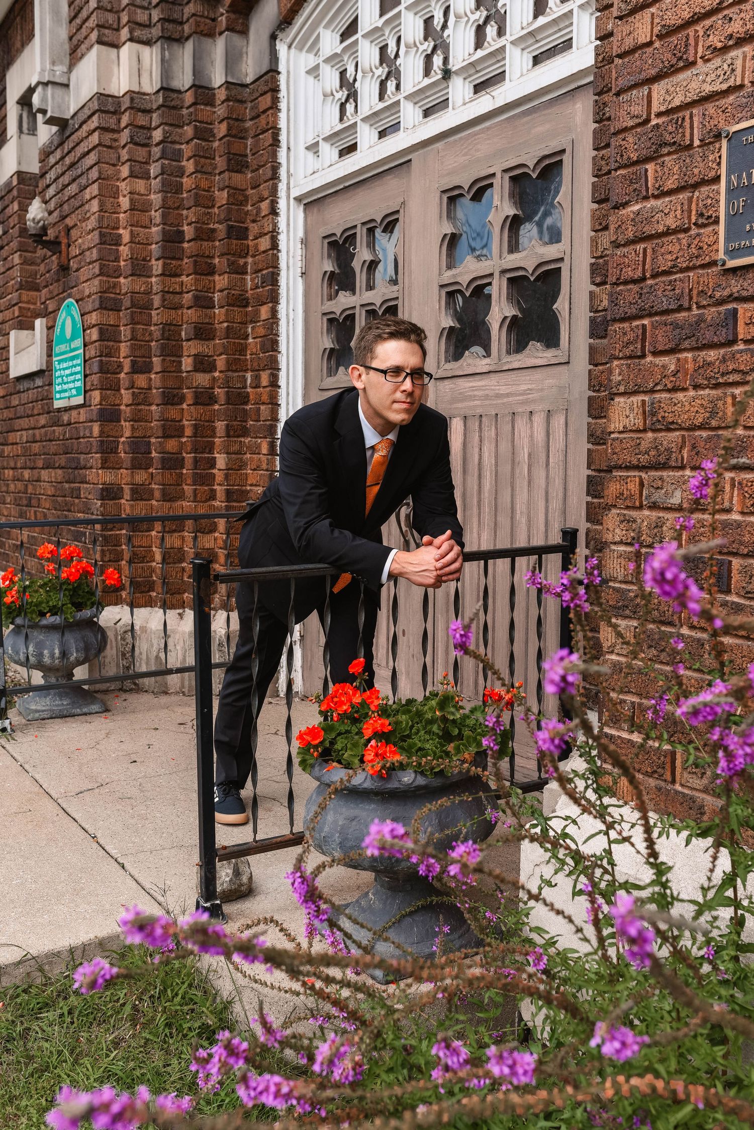 Playful poses captured near colorful flowers outside a brick building entrance.