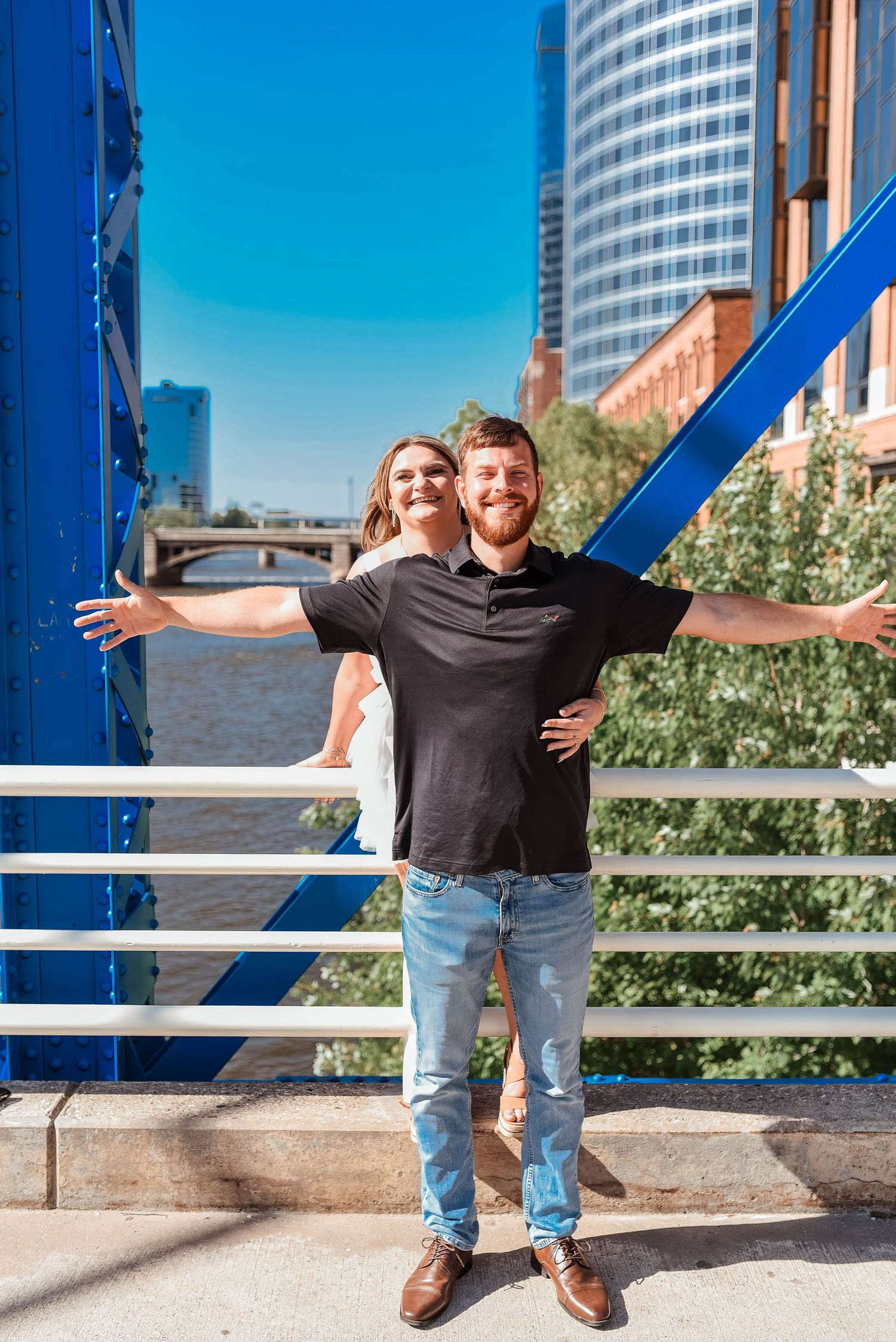 A couple strikes fun poses on a blue railing with city skyline behind them.