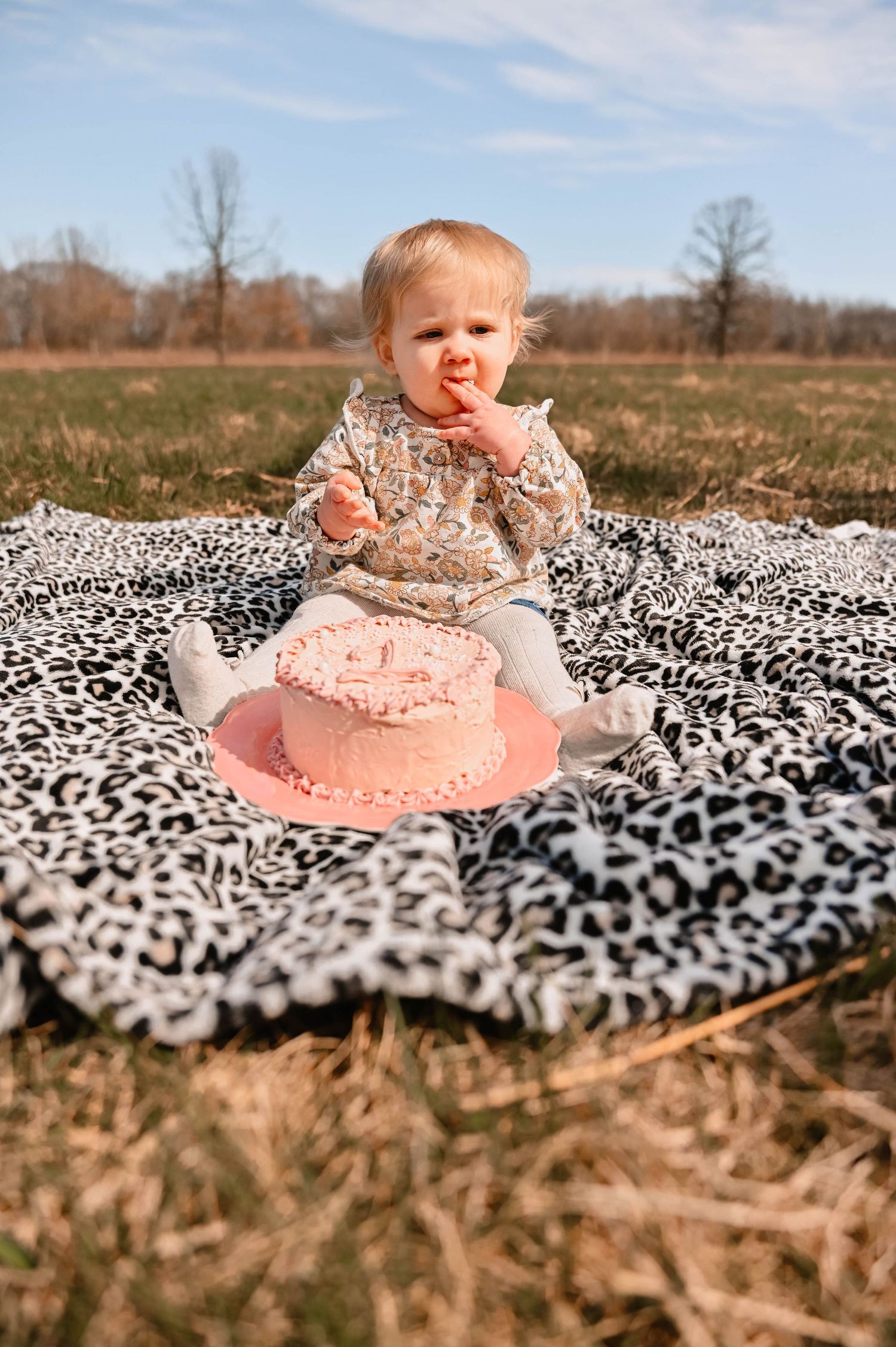 Baby in pink dress lying on black and white patterned blanket outdoors.