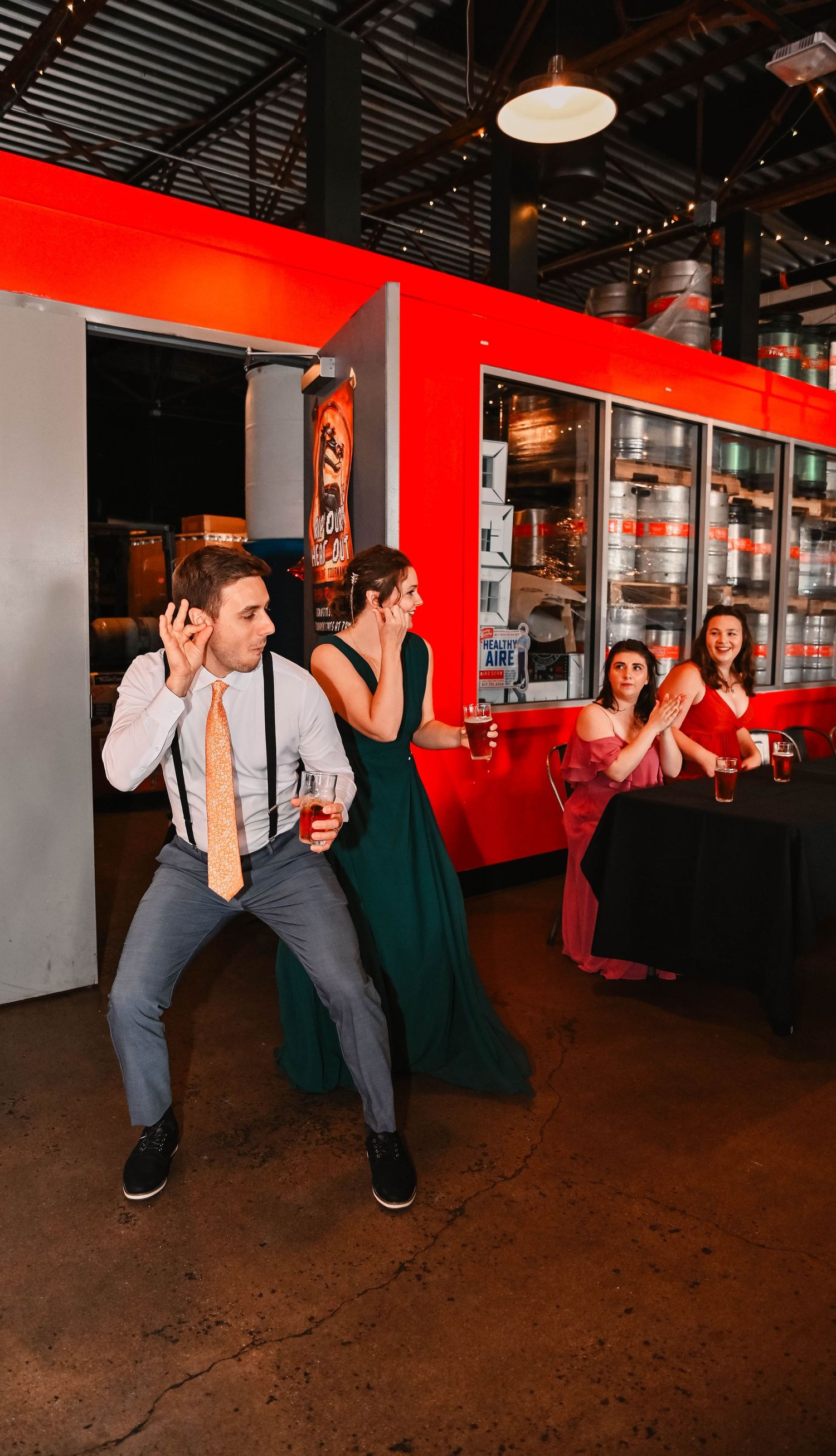 Wedding guests dance in formation at brewery reception with red accent lighting.
