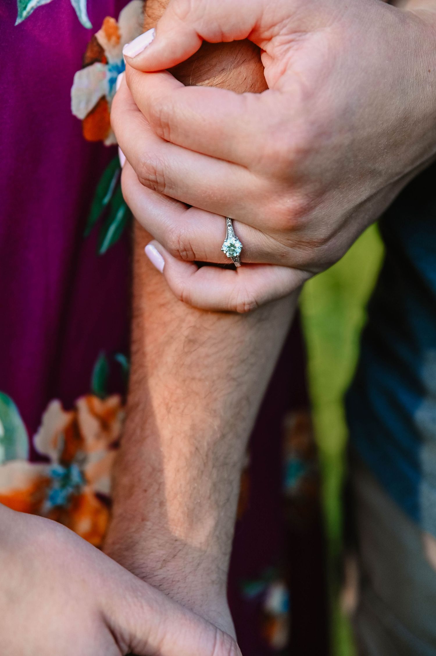 Close-up of hands showing engagement ring against purple background.